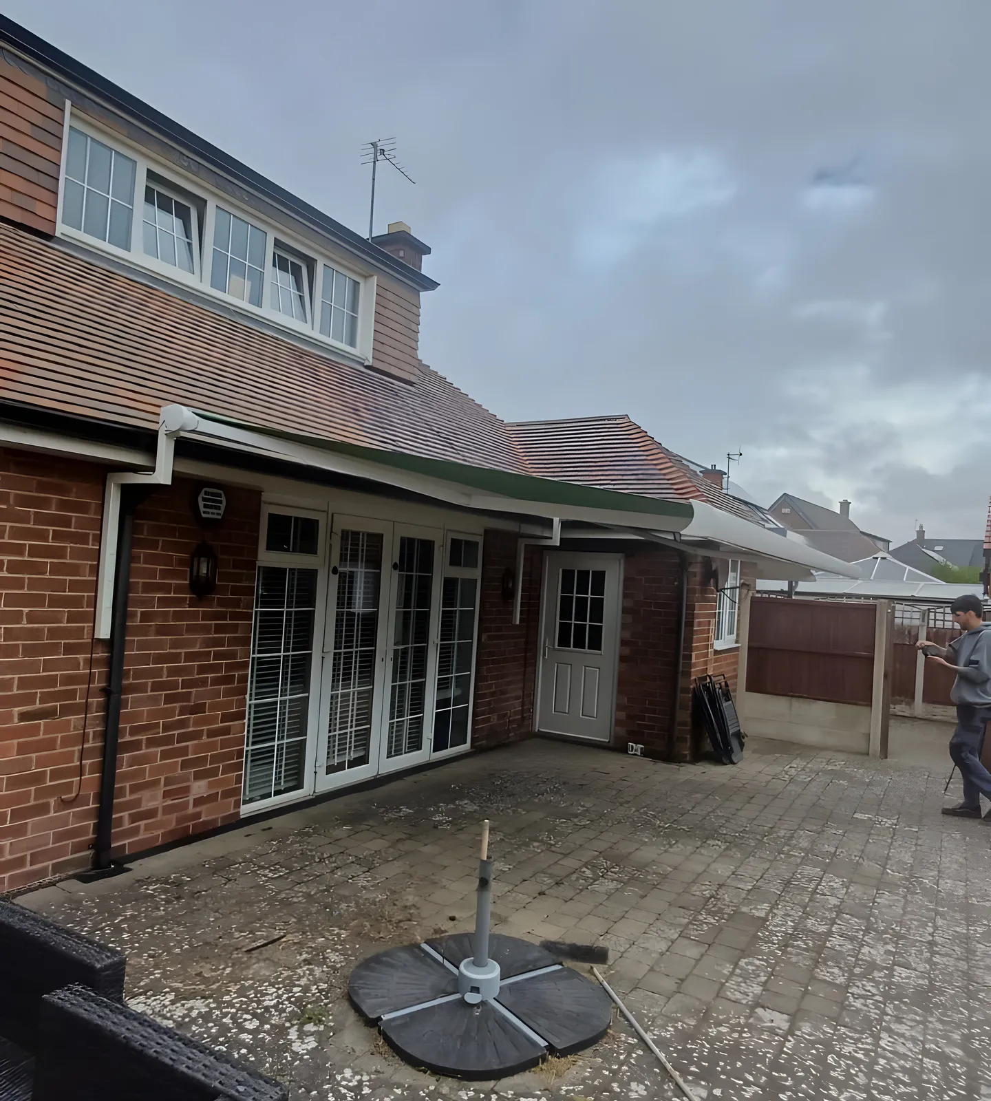 Green retractable awning extended over patio doors at the back of a brick house