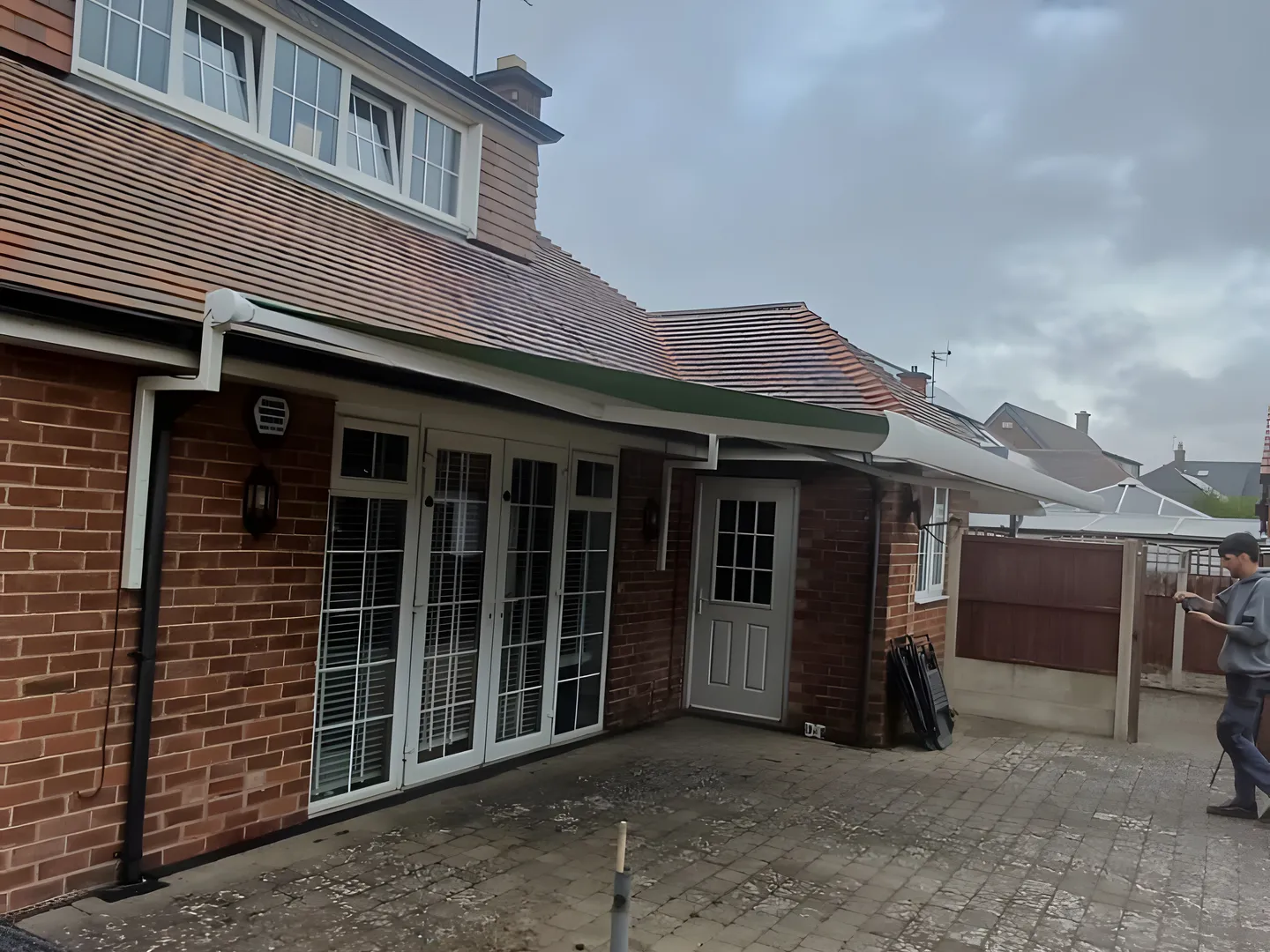 Green retractable awning extended over patio doors at the back of a brick house