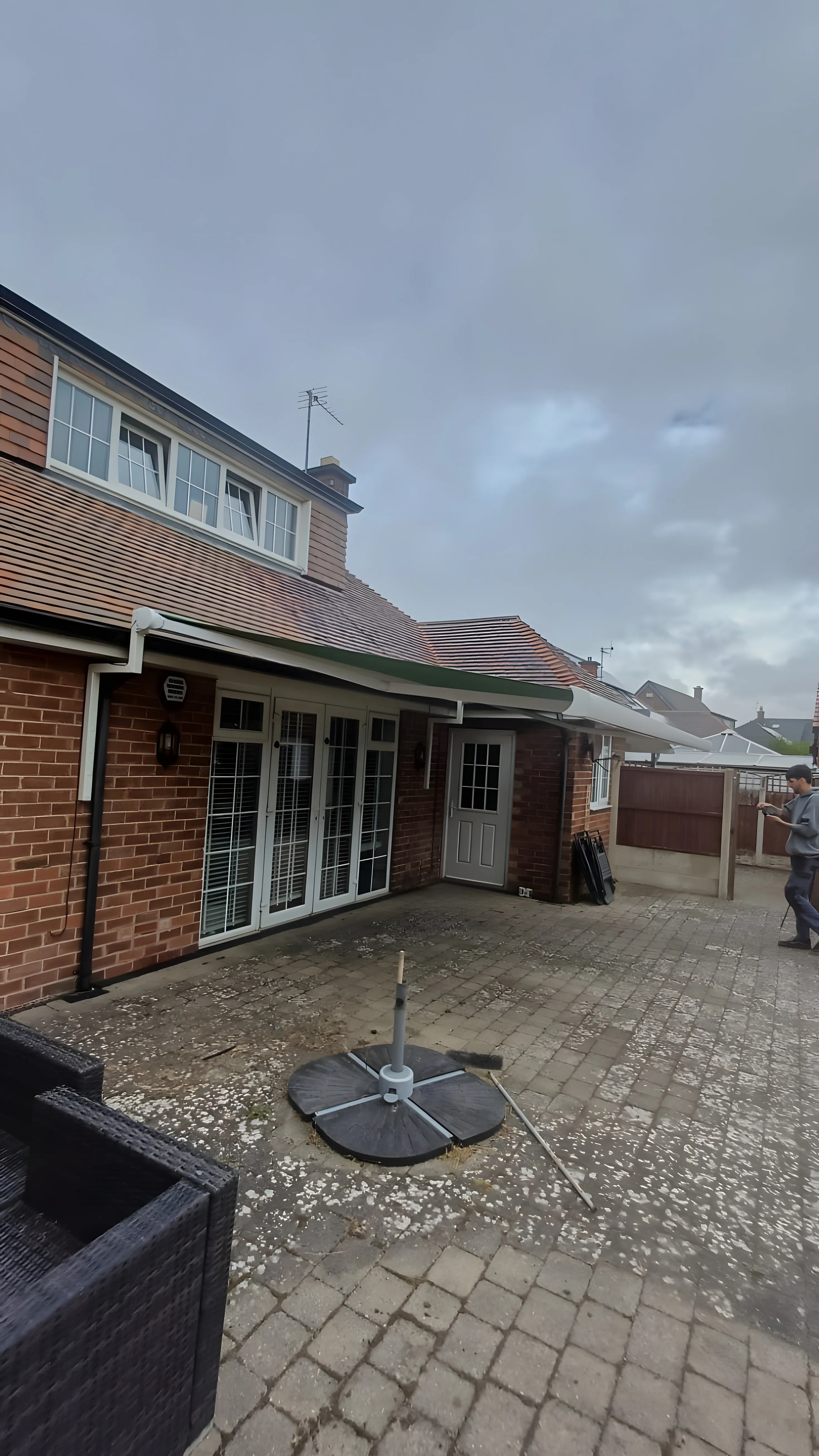 Green retractable awning extended over patio doors at the back of a brick house