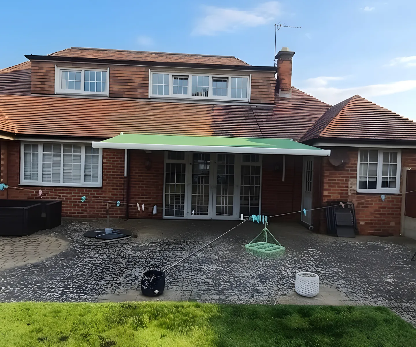 Green awning fitted above the rear doors of a semi-detached house, seen from the garden