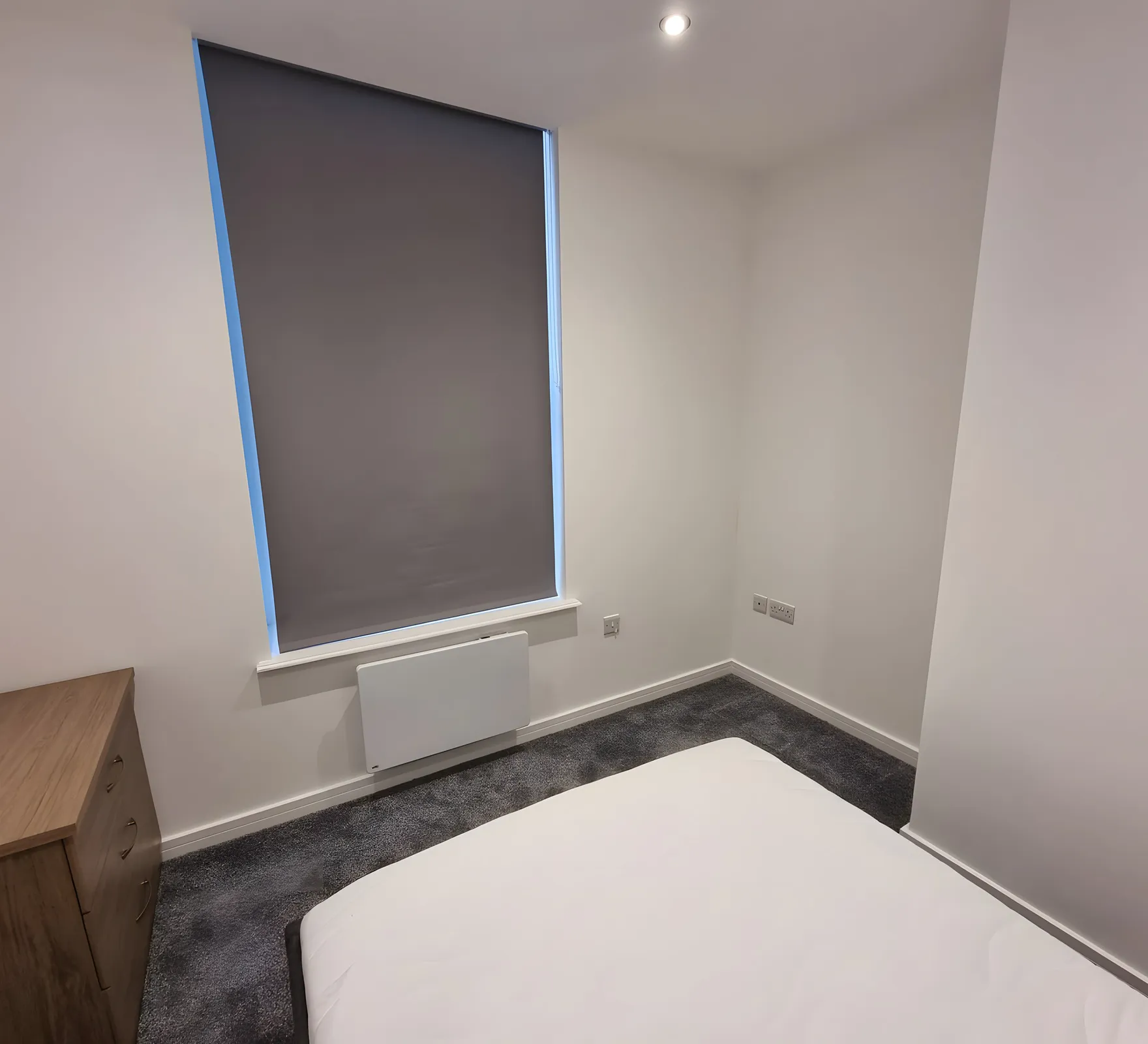 Blackout roller blind lowered over the window of a new resident bedroom at Beech House Care Home, bed and chest of drawers in place