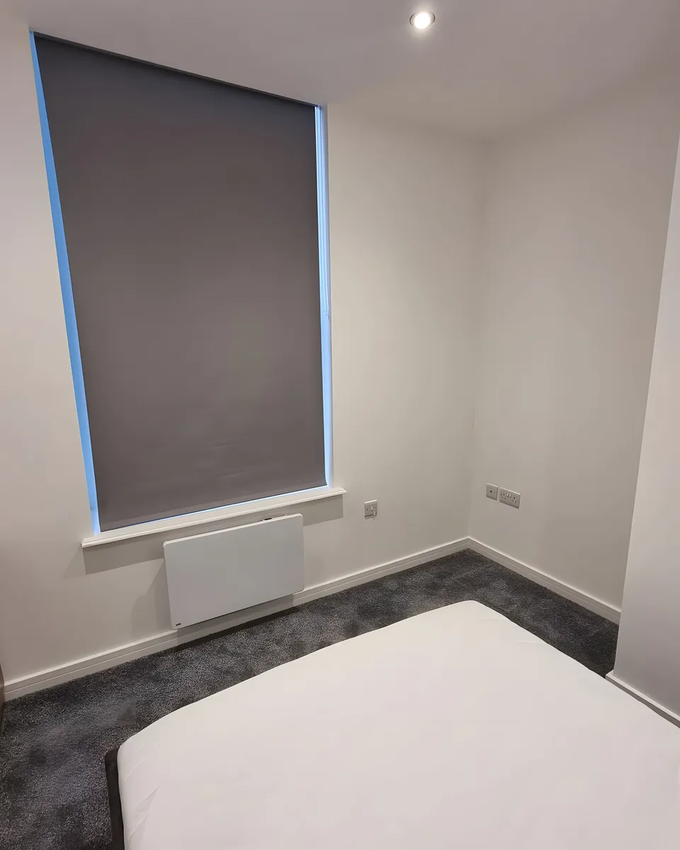Blackout roller blind lowered over the window of a new resident bedroom at Beech House Care Home, bed and chest of drawers in place