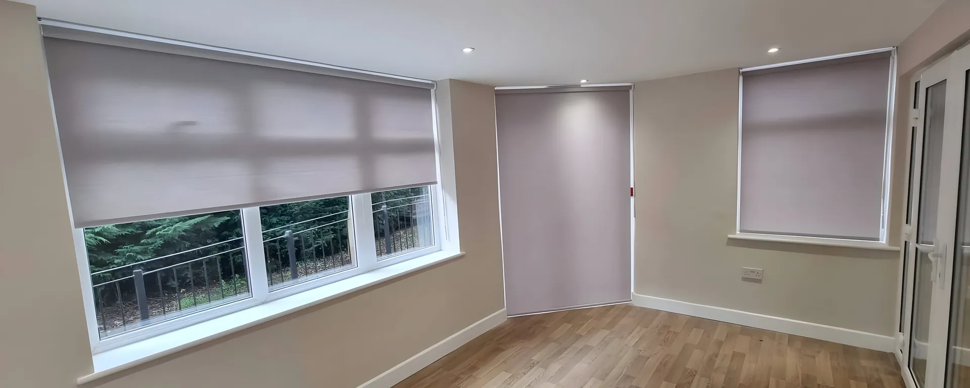Dim-out roller blinds half lowered across a run of windows in a bright day room at Beech House Care Home, wood-effect floor below