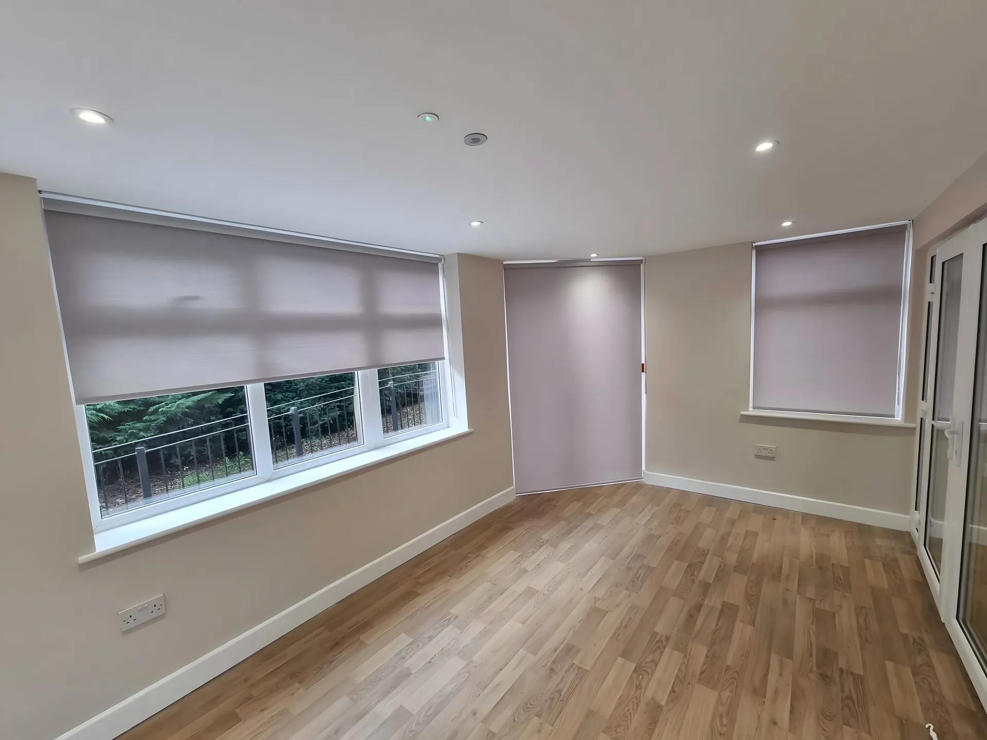 Dim-out roller blinds half lowered across a run of windows in a bright day room at Beech House Care Home, wood-effect floor below
