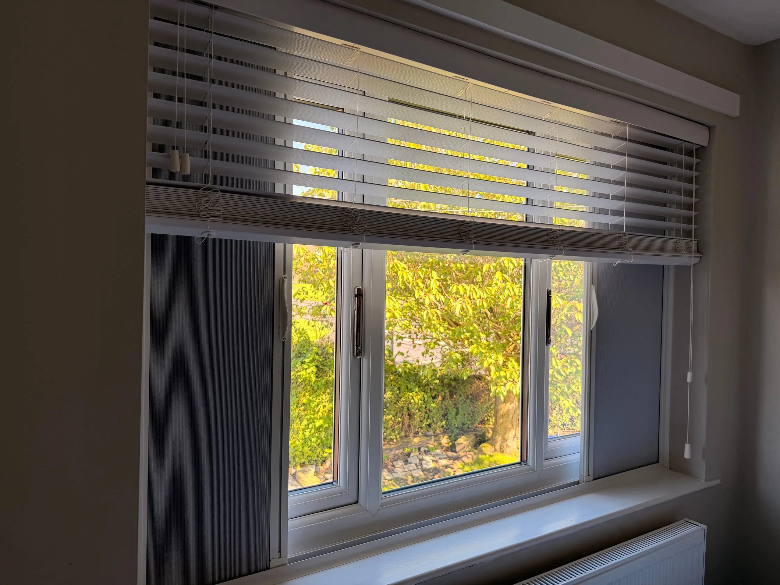 Blind Screen blackout screens parked at each side of a bedroom window beneath a white Venetian blind