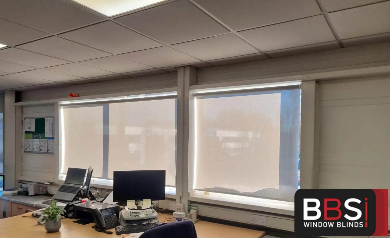 Screen fabric roller blinds down behind a desk and monitors at Building Technology Systems, room still bright with the glare gone