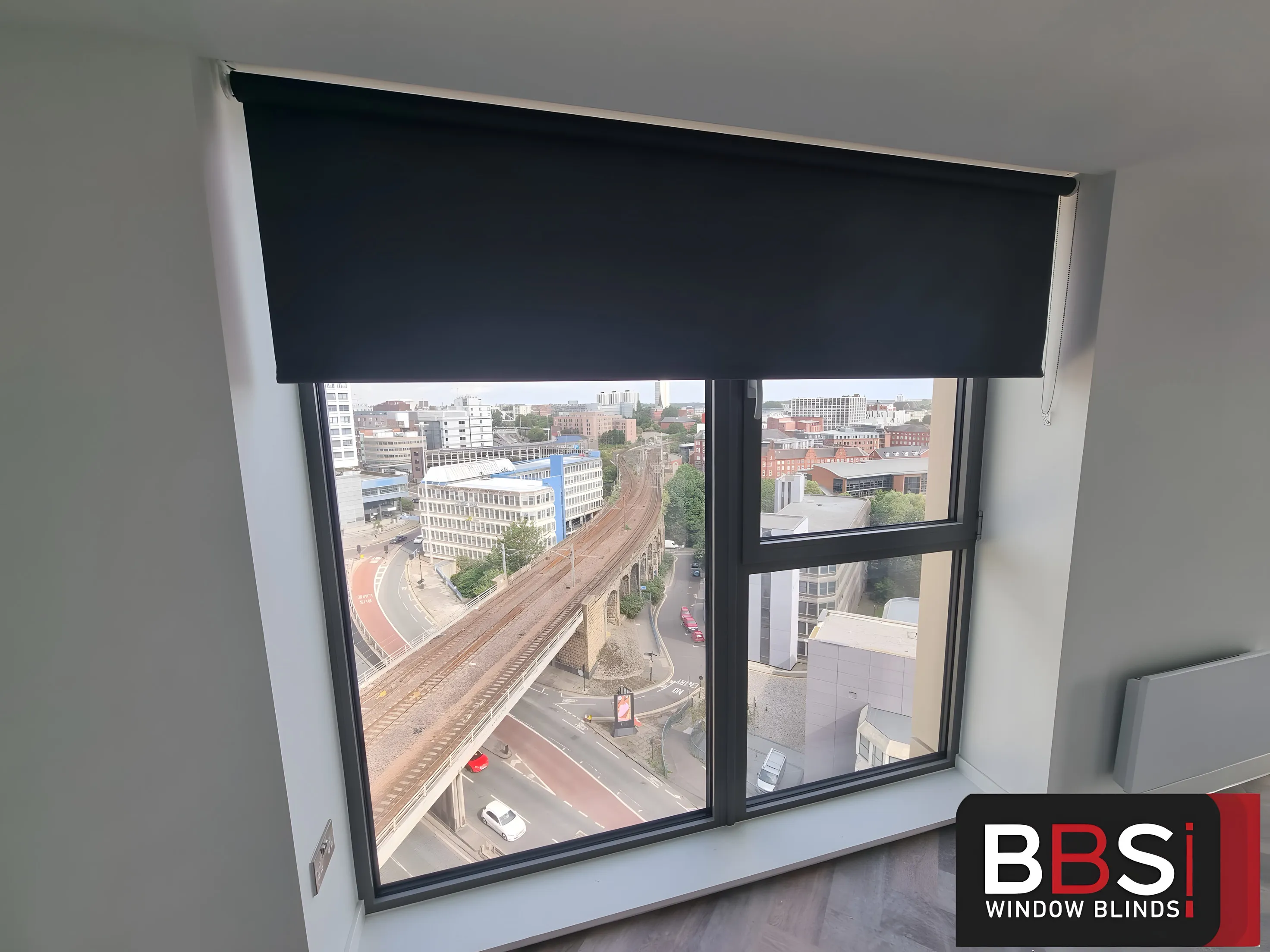 Navy roller blind half lowered over an apartment window at Cale Cross with a high view across Newcastle and the railway viaduct