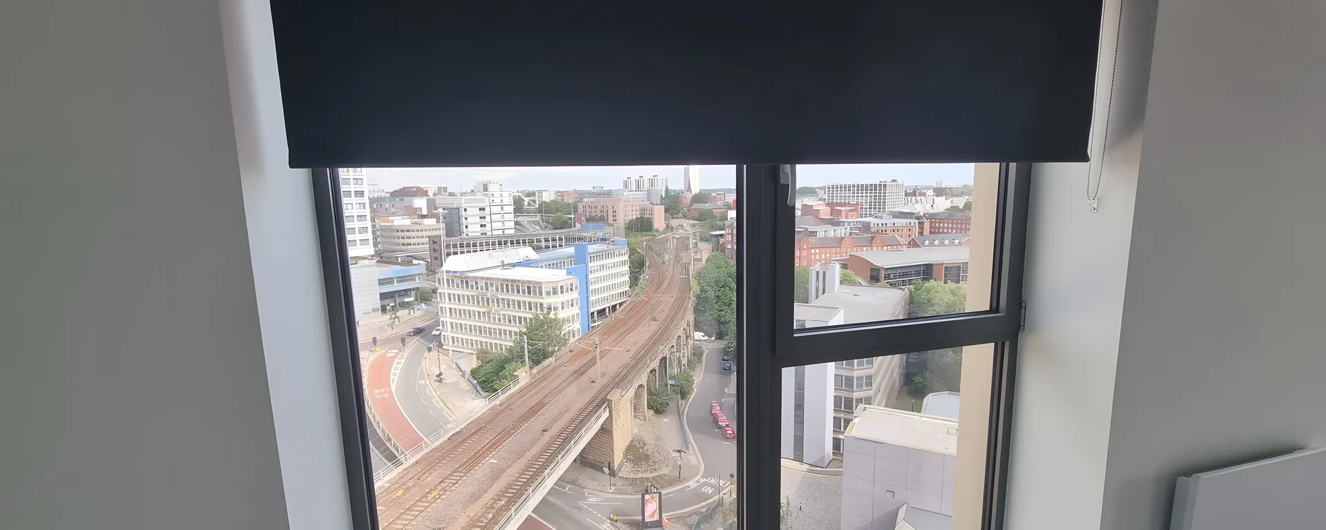 Navy roller blind half lowered over an apartment window at Cale Cross with a high view across Newcastle and the railway viaduct