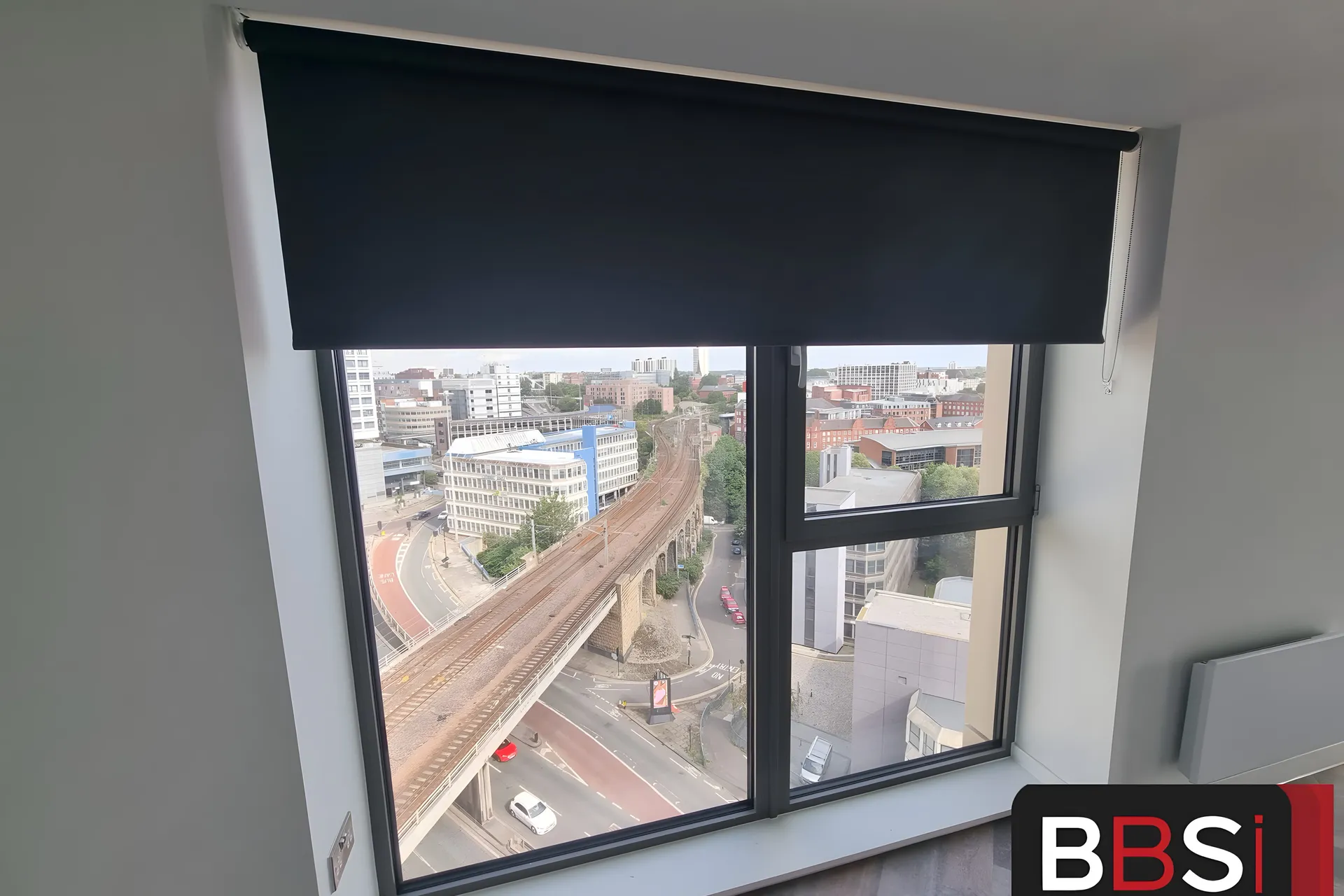 Navy roller blind half lowered over an apartment window at Cale Cross with a high view across Newcastle and the railway viaduct