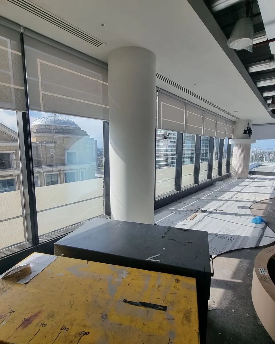 Screen fabric roller blinds along the perimeter glazing of a Canary Wharf office floor mid fit-out, floor protection down and joinery still being built