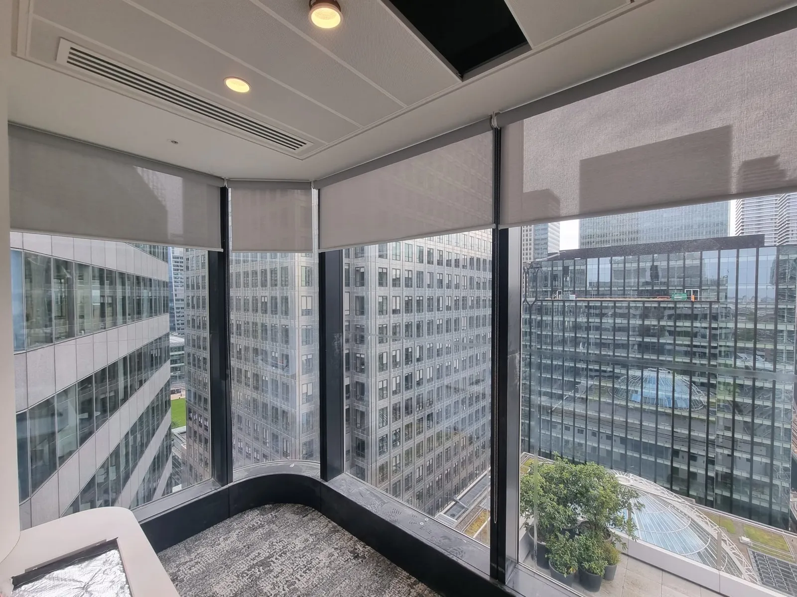 Screen fabric roller blinds on each faceted pane of a curved curtain wall corner at Canary Wharf