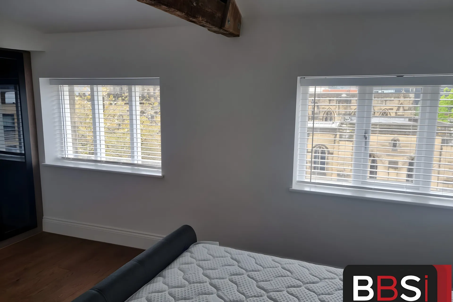 White Venetian blinds fitted to two windows of a new apartment at Cathedral View in Sheffield, exposed timber beam above the bed
