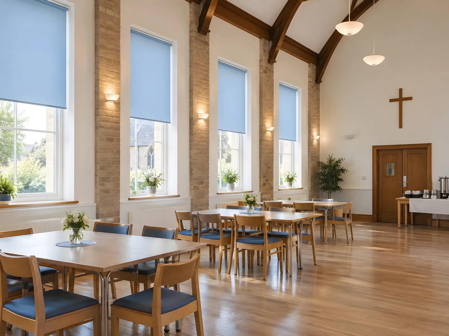 Pale blue roller blinds at tall windows in a furnished church community hall