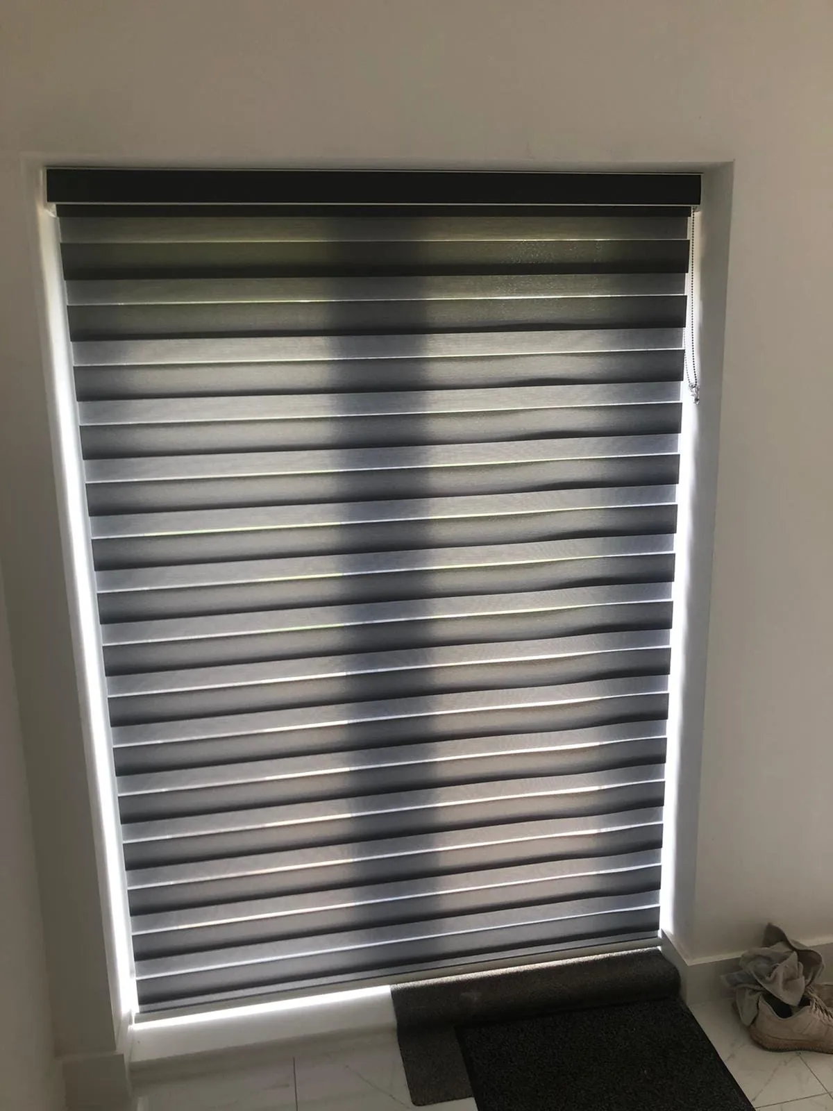 Charcoal day and night blind lowered over a hallway window, with daylight at the edges