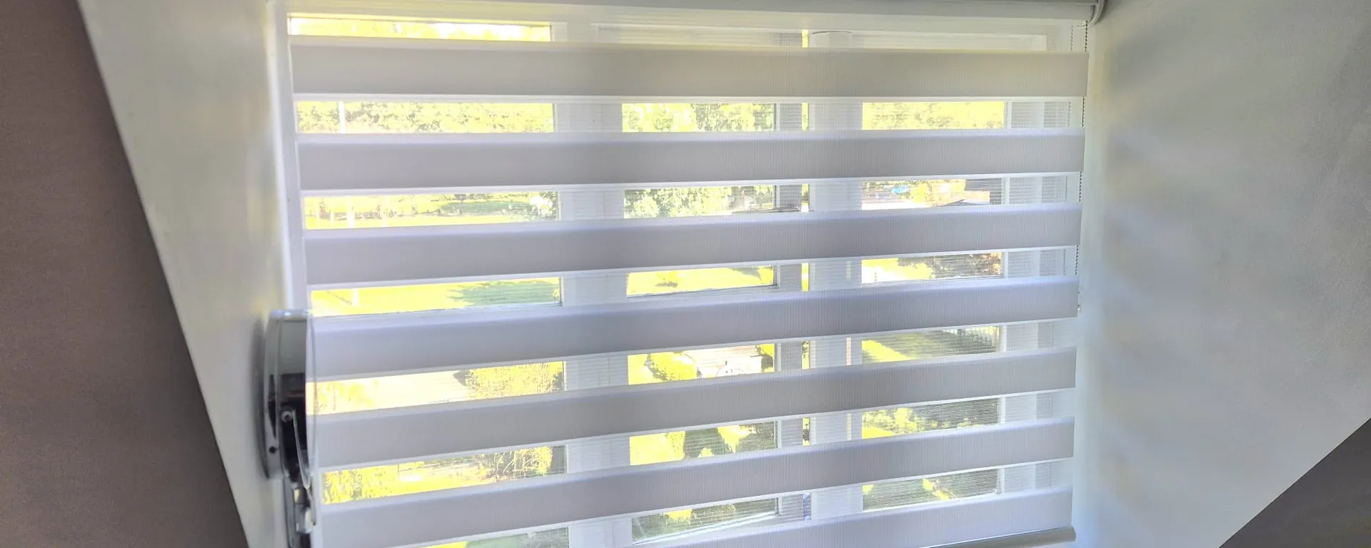 White day and night blind on a loft bathroom window, with the garden showing through the sheer bands