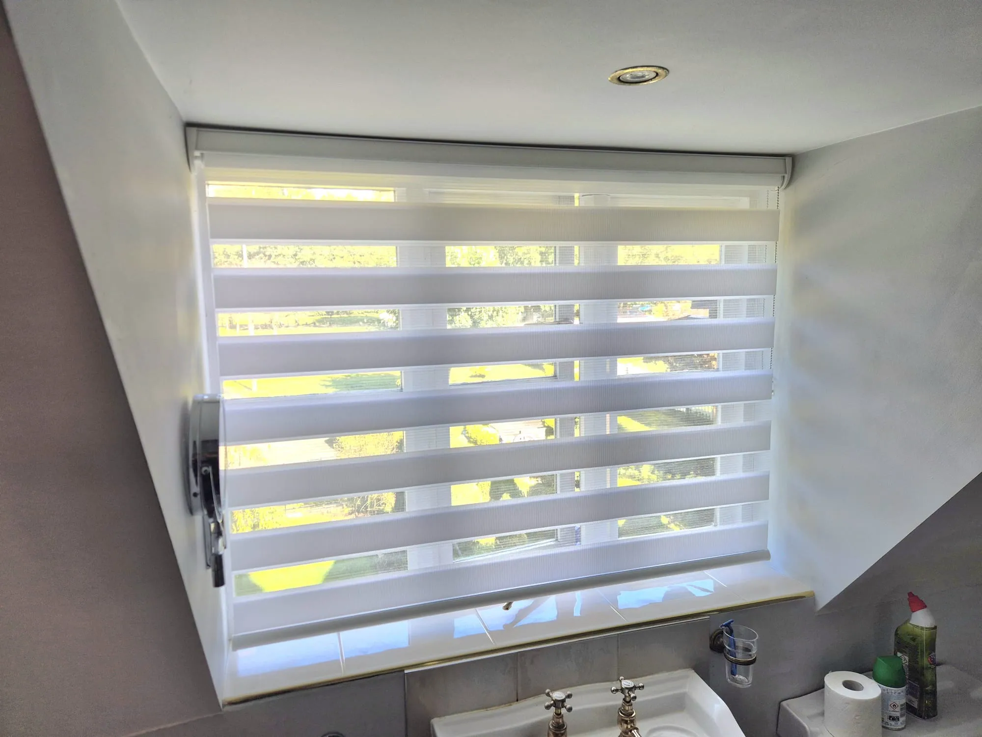 White day and night blind on a loft bathroom window, with the garden showing through the sheer bands