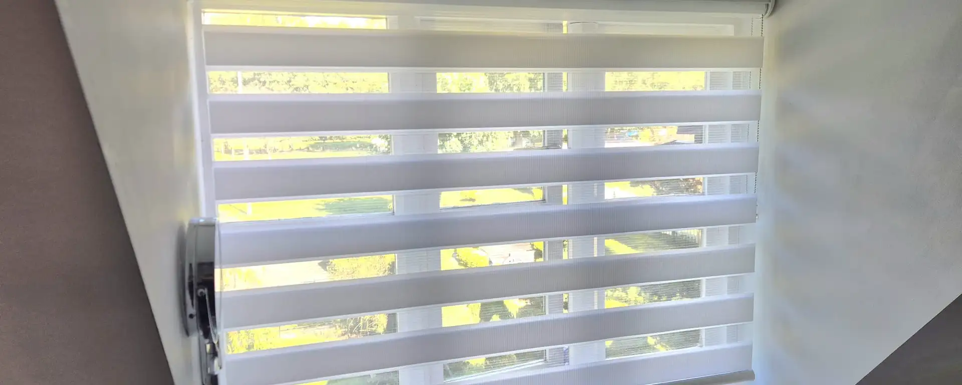 White day and night blind on a loft bathroom window, with the garden showing through the sheer bands