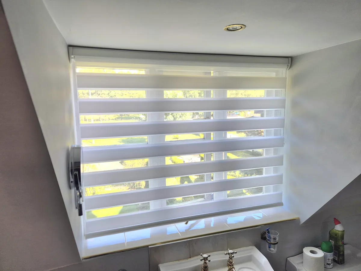 White day and night blind on a loft bathroom window, with the garden showing through the sheer bands