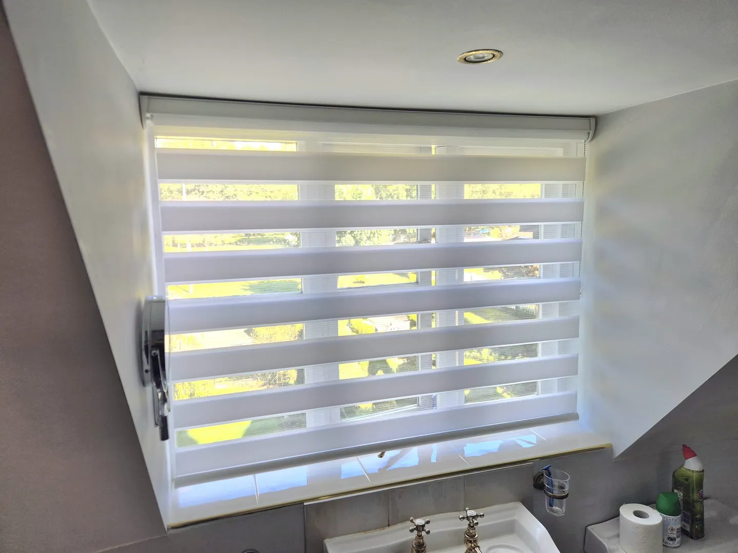 White day and night blind on a loft bathroom window, with the garden showing through the sheer bands