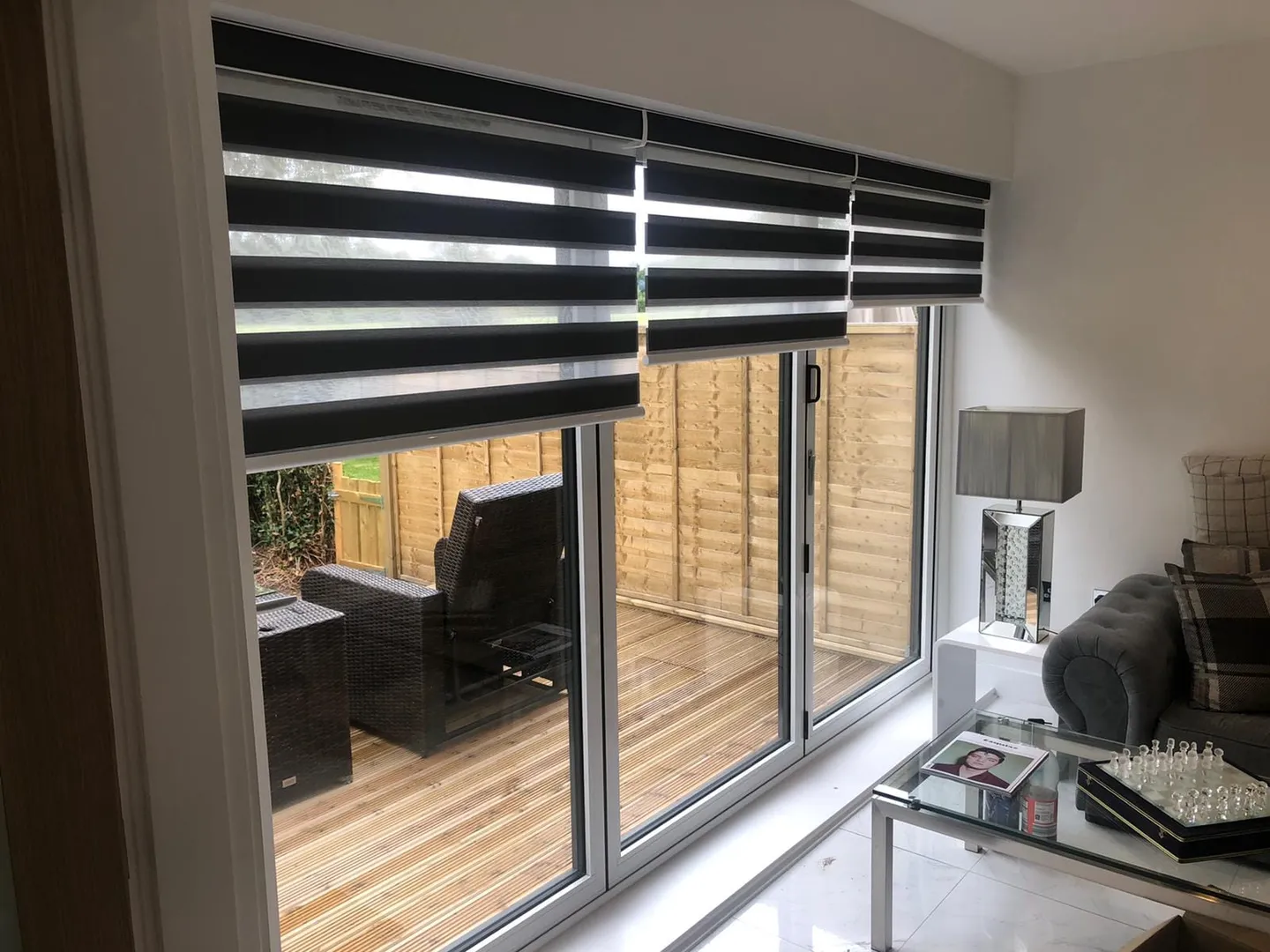 White day and night blind half lowered across patio doors, with the garden deck beyond