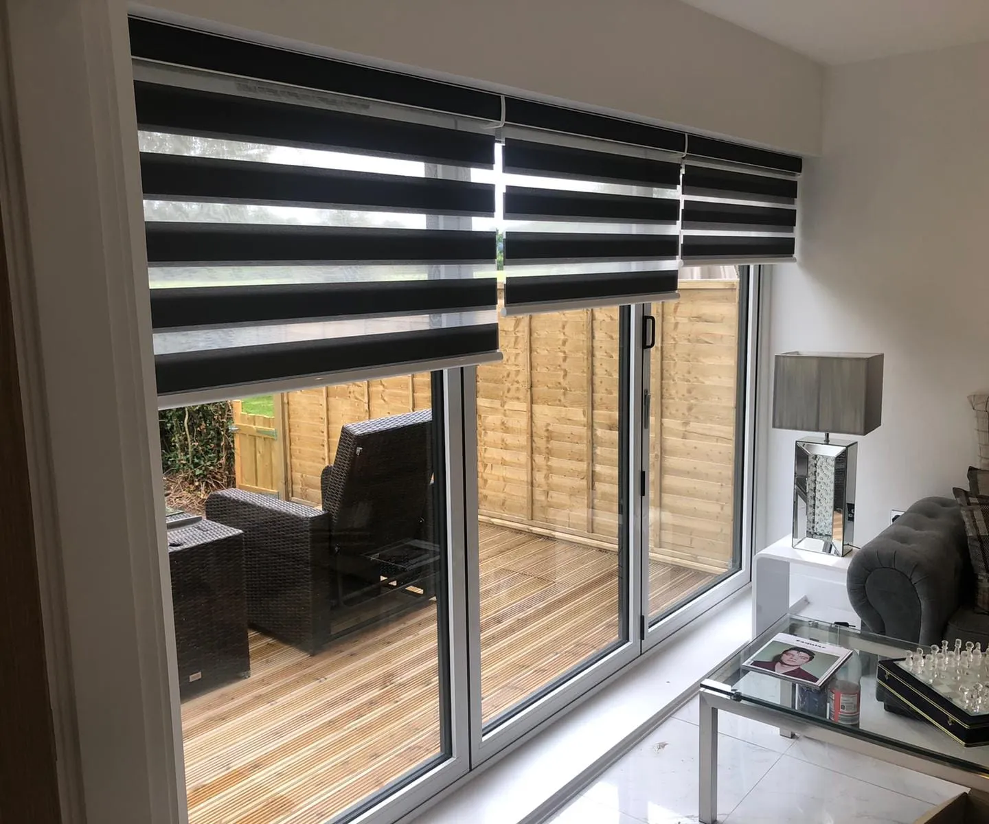 White day and night blind half lowered across patio doors, with the garden deck beyond
