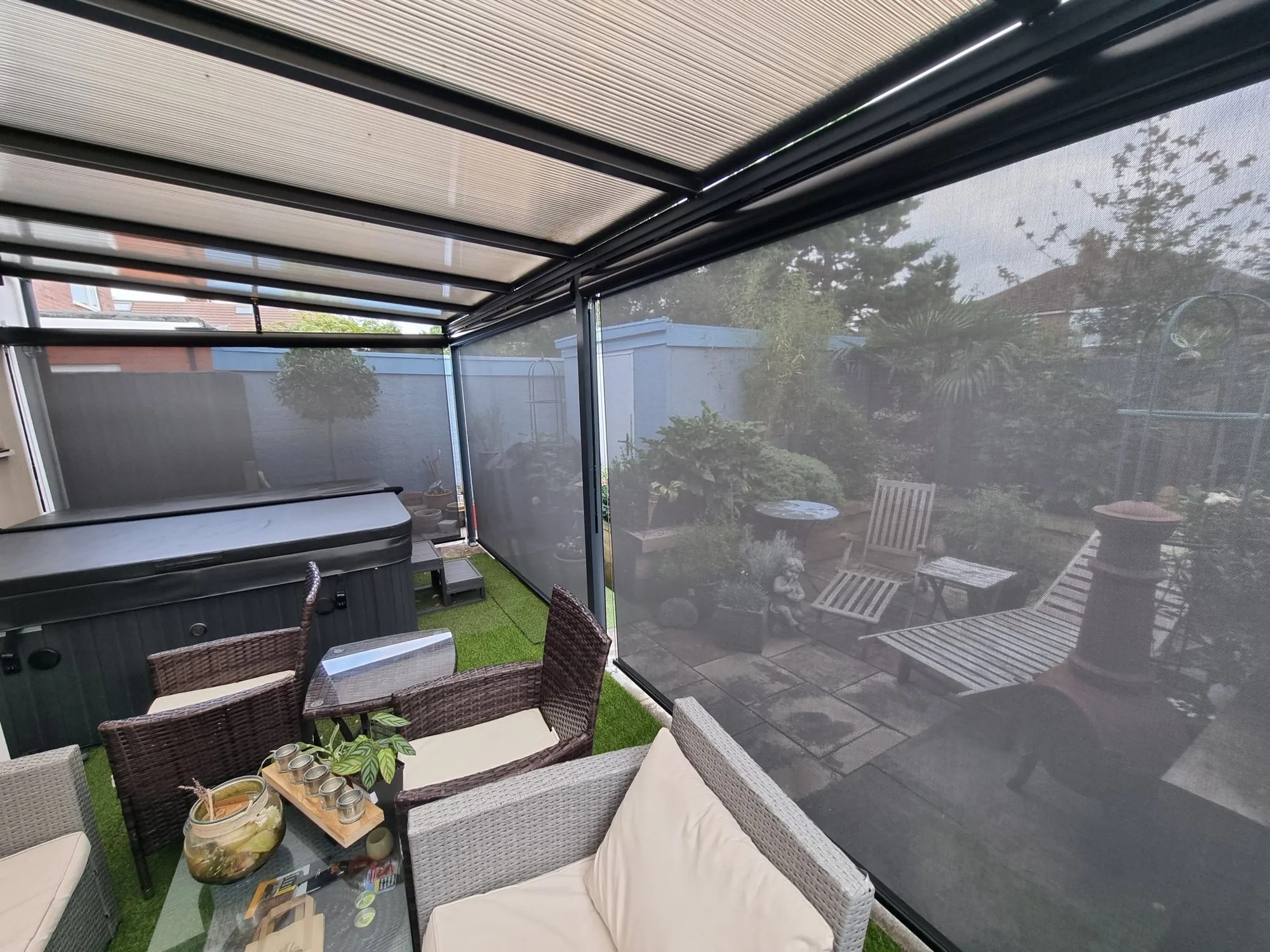 Grey external screen blinds lowered on a garden pergola beside a hot tub and seating