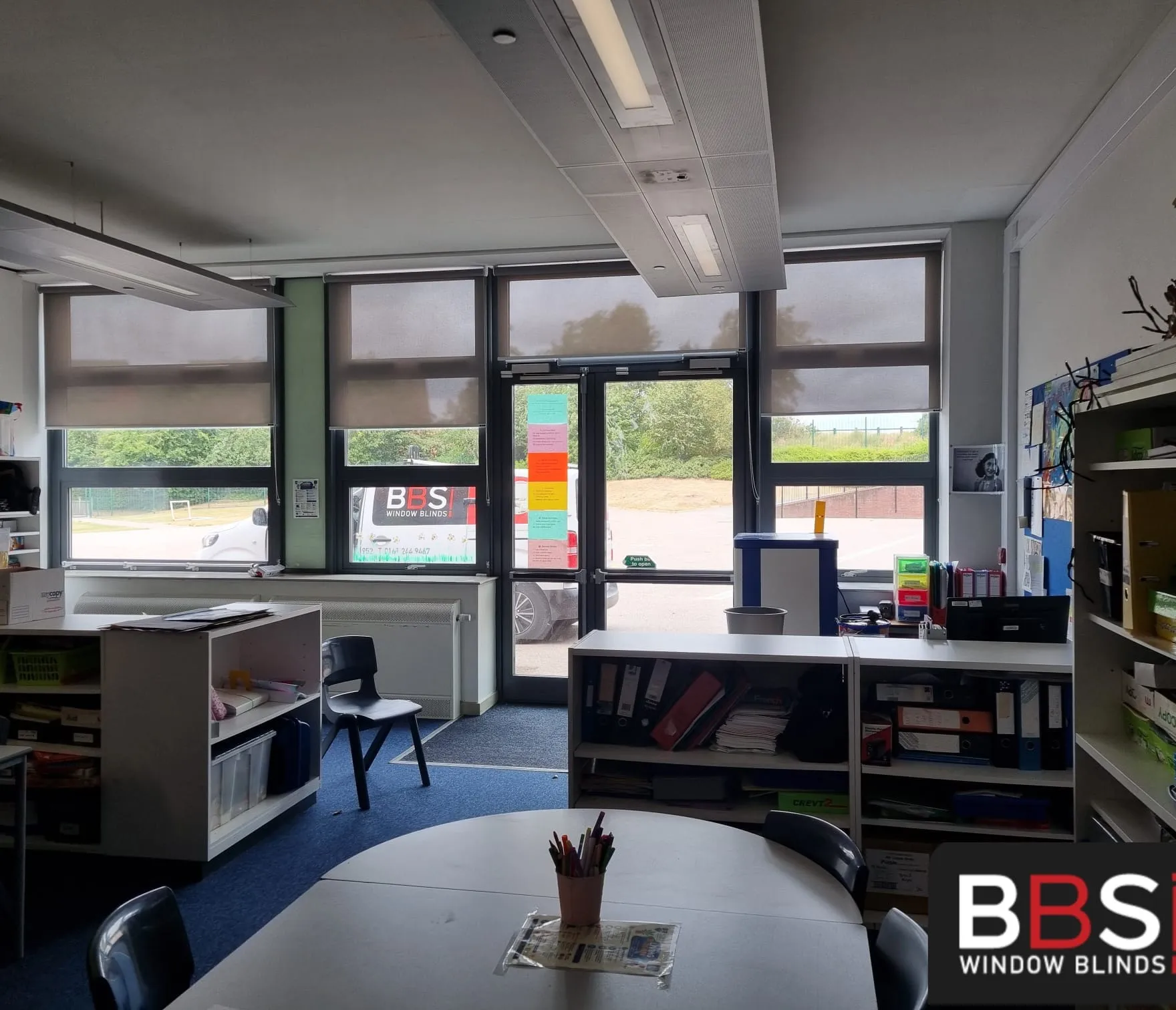 Grey roller blinds on a classroom window run at The Grange Academy, with the BBS van visible through the glass