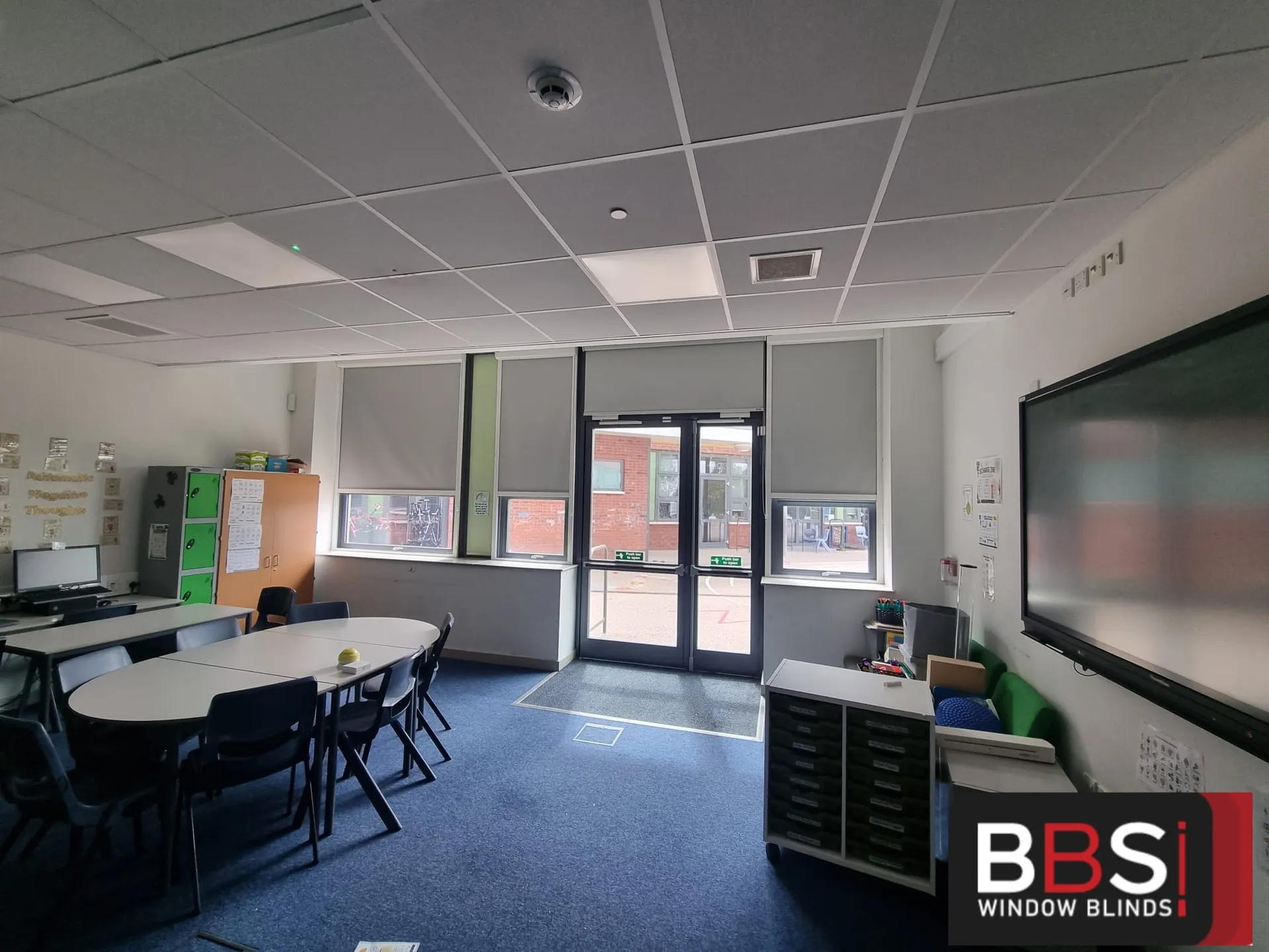 Grey roller blinds across classroom windows and the glazed external doors at The Grange Academy, oval tables in the foreground