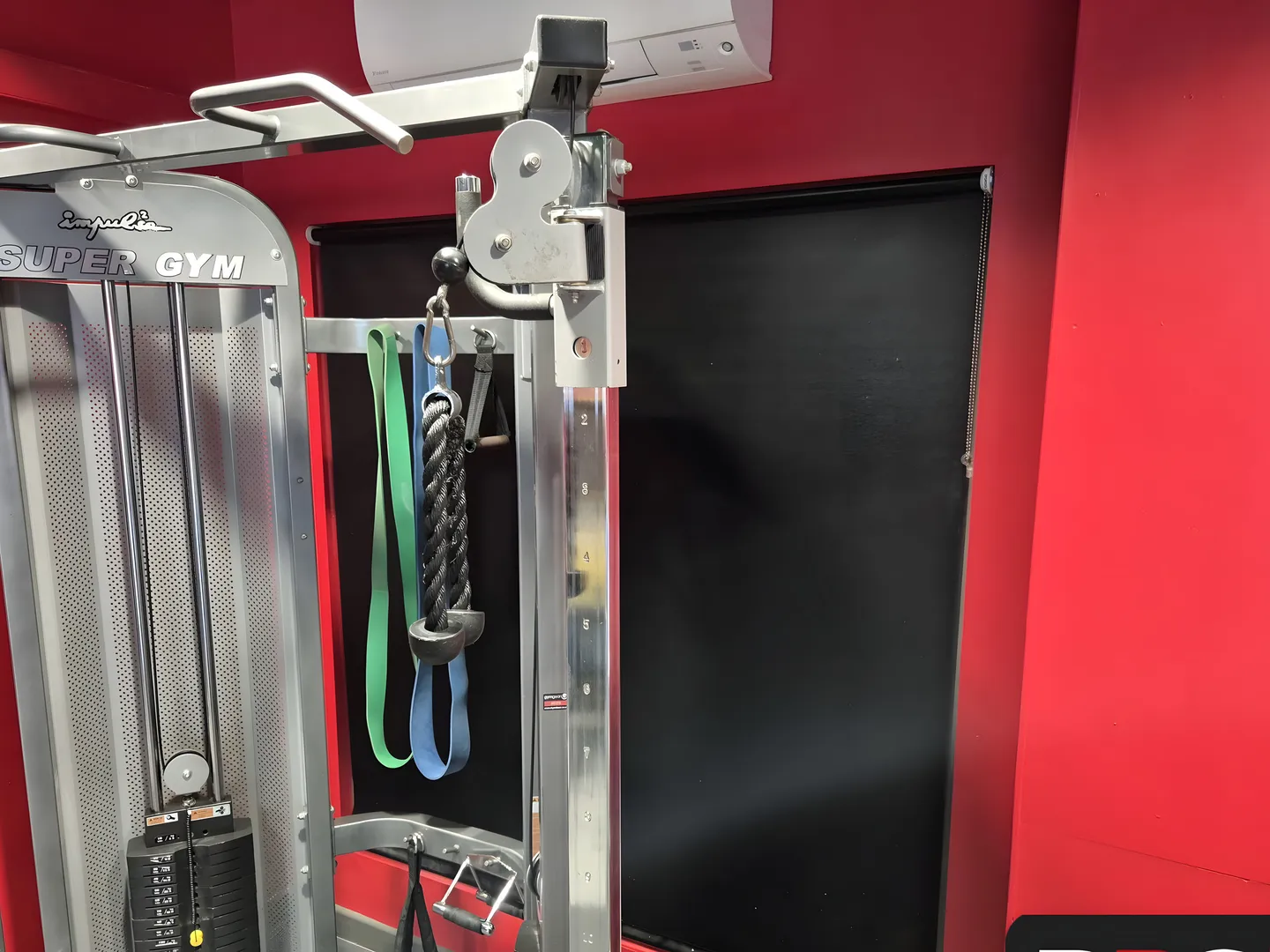 Blackout roller blind fitted beside a cable machine in a red-walled gym