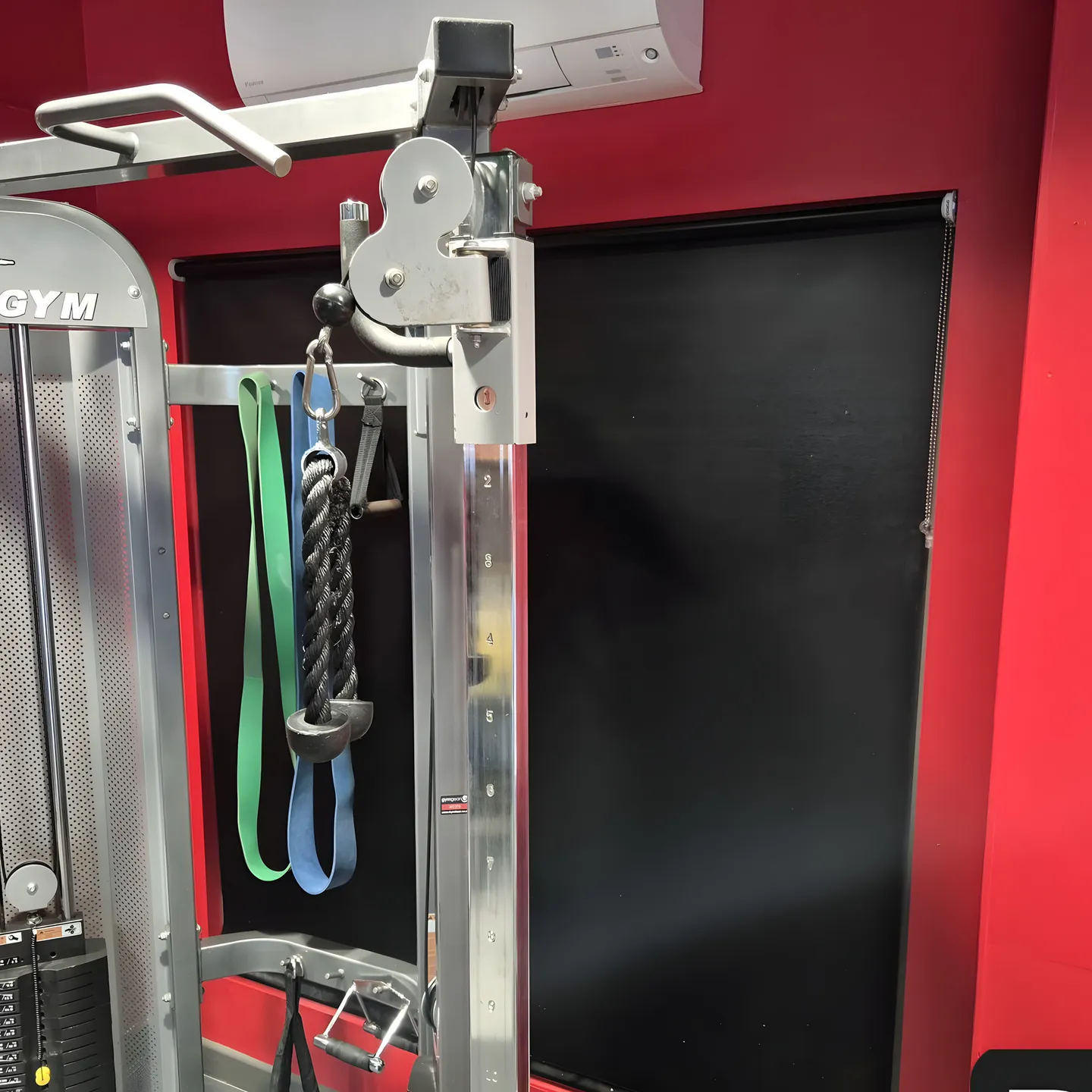 Blackout roller blind lowered beside a cable machine in a red-walled gym
