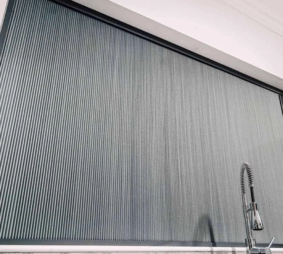 Close view of a grey Blind Screen honeycomb blind filling its slim frame at a kitchen window
