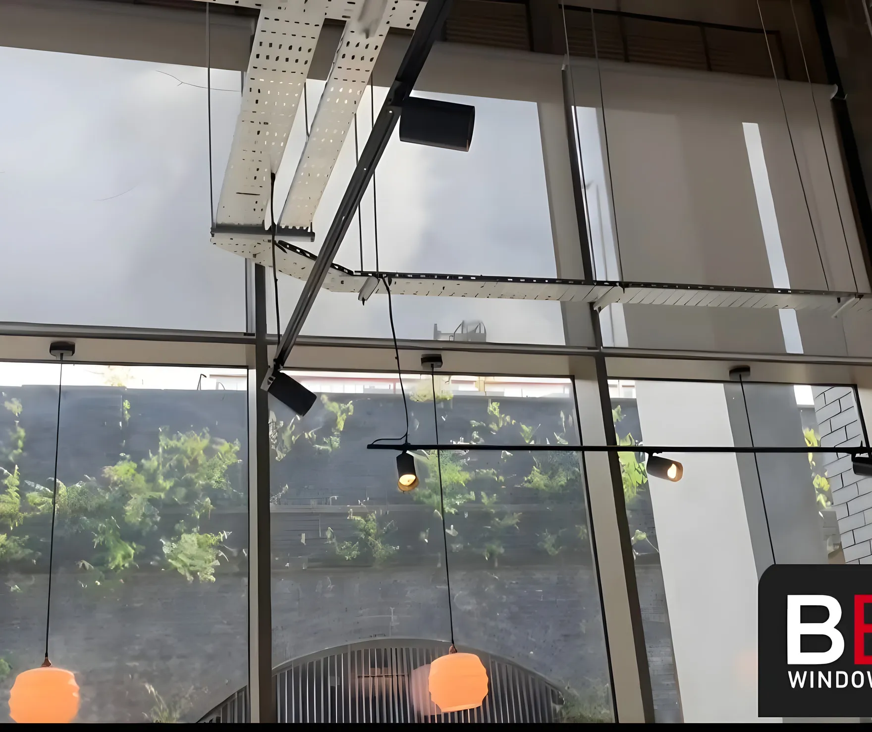 Screen fabric blinds part lowered above the greenery outside Inner West cafe, orange pendant lights hanging in front