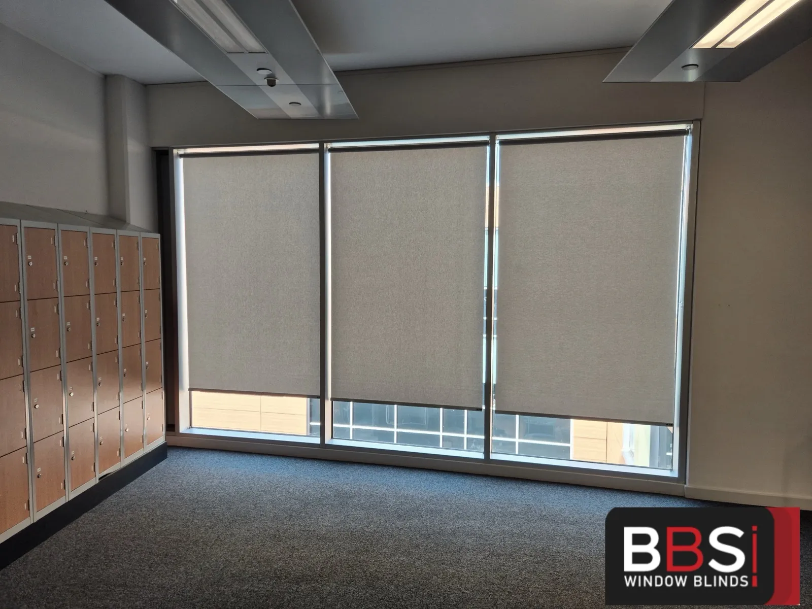 Three matching roller blinds across a full window wall next to a bank of lockers