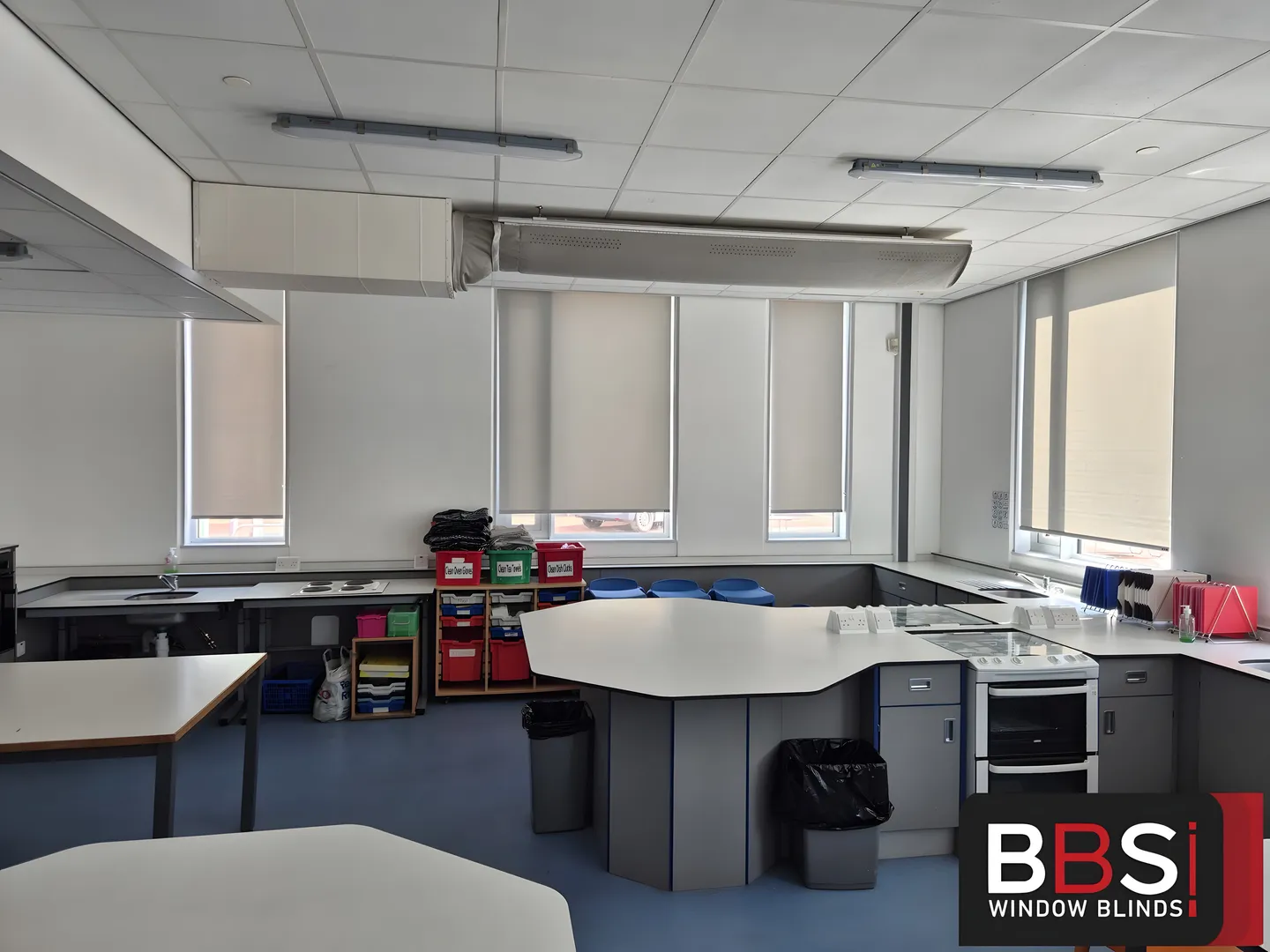Pale roller blinds fitted around the sinks, cookers and worktops of a secondary school food technology room in Salford