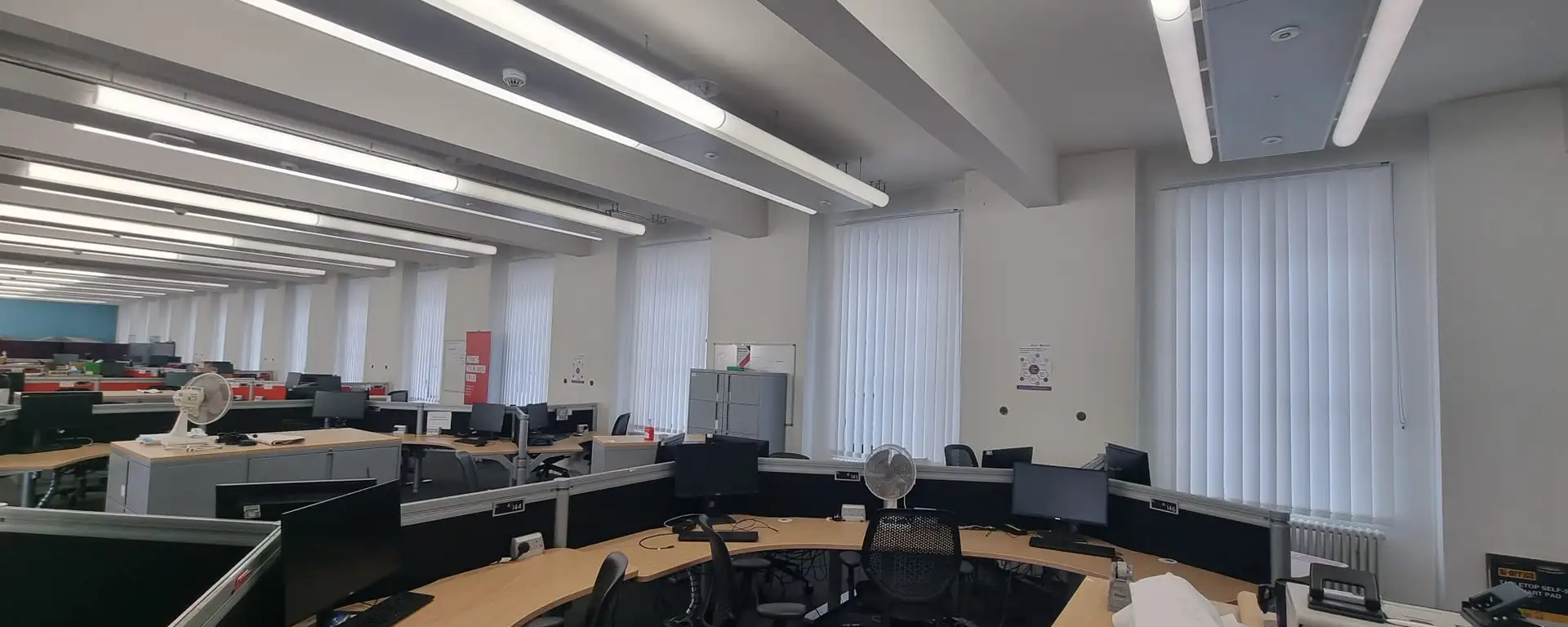 White vertical blinds along a civic office window run at Manchester Town Hall, with curved desks and workstations in the foreground