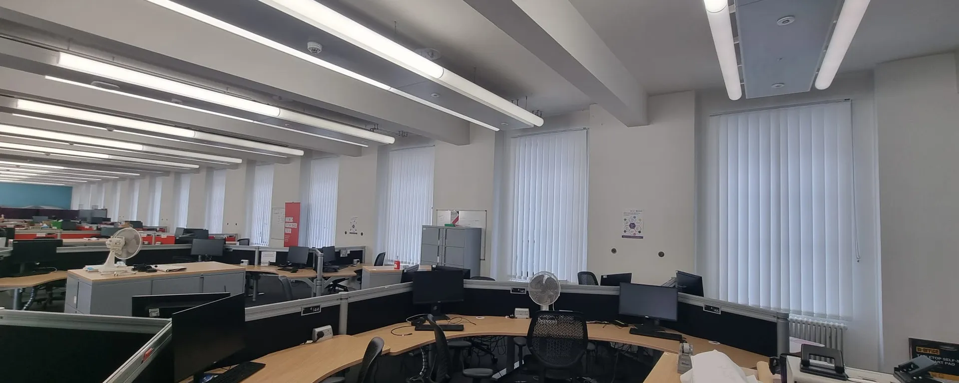White vertical blinds along a civic office window run at Manchester Town Hall, with curved desks and workstations in the foreground
