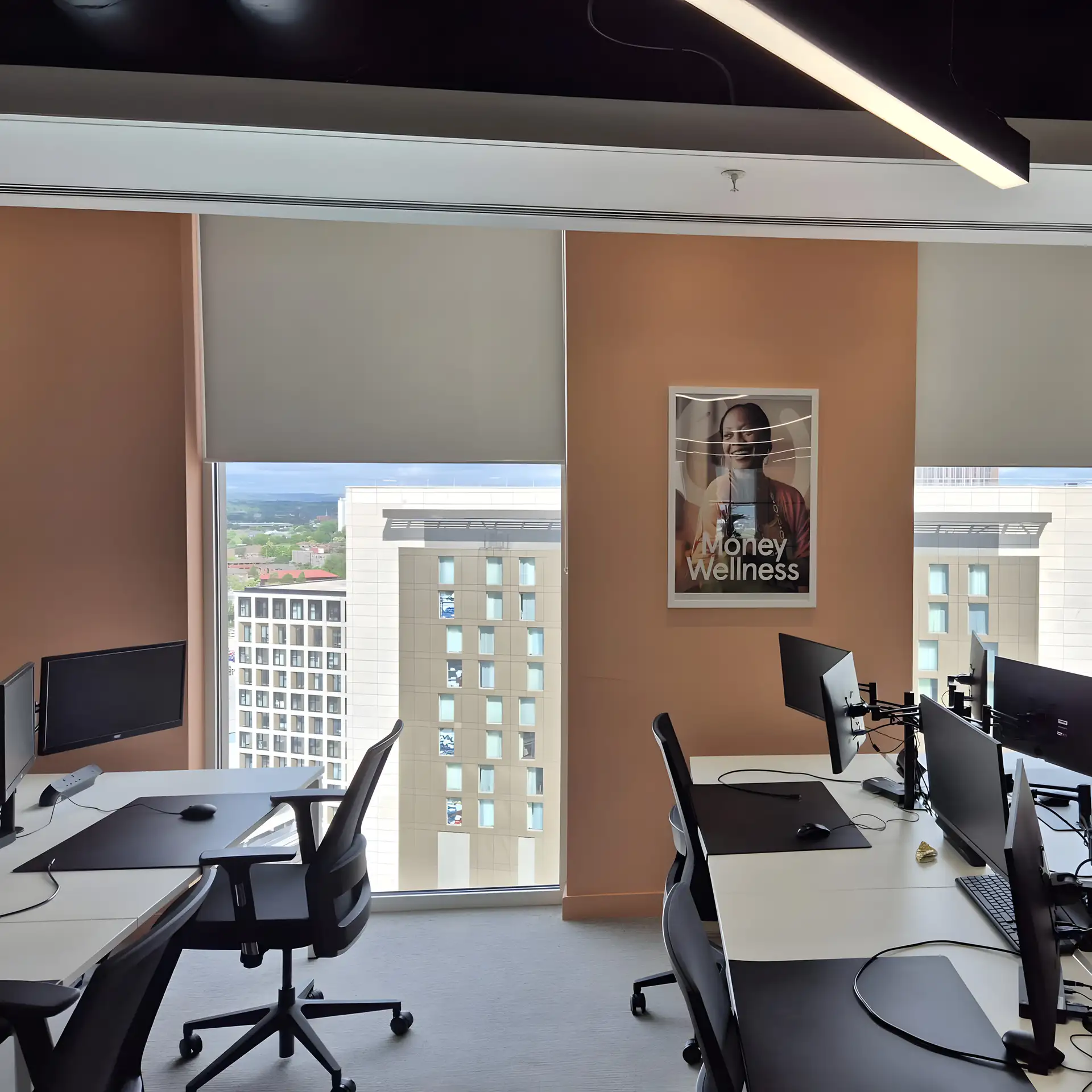 Pale roller blinds fitted by BBS at Money Wellness in Salford Quays, with office desks and nearby buildings visible