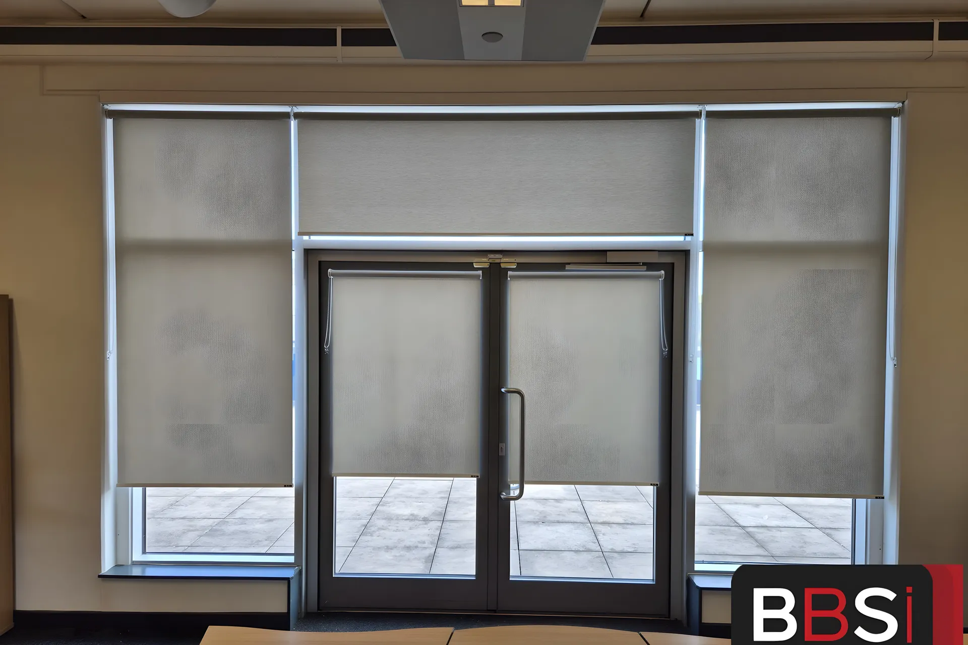 Wall of matching dim-out roller blinds either side of a glazed fire exit door at Moorside High School
