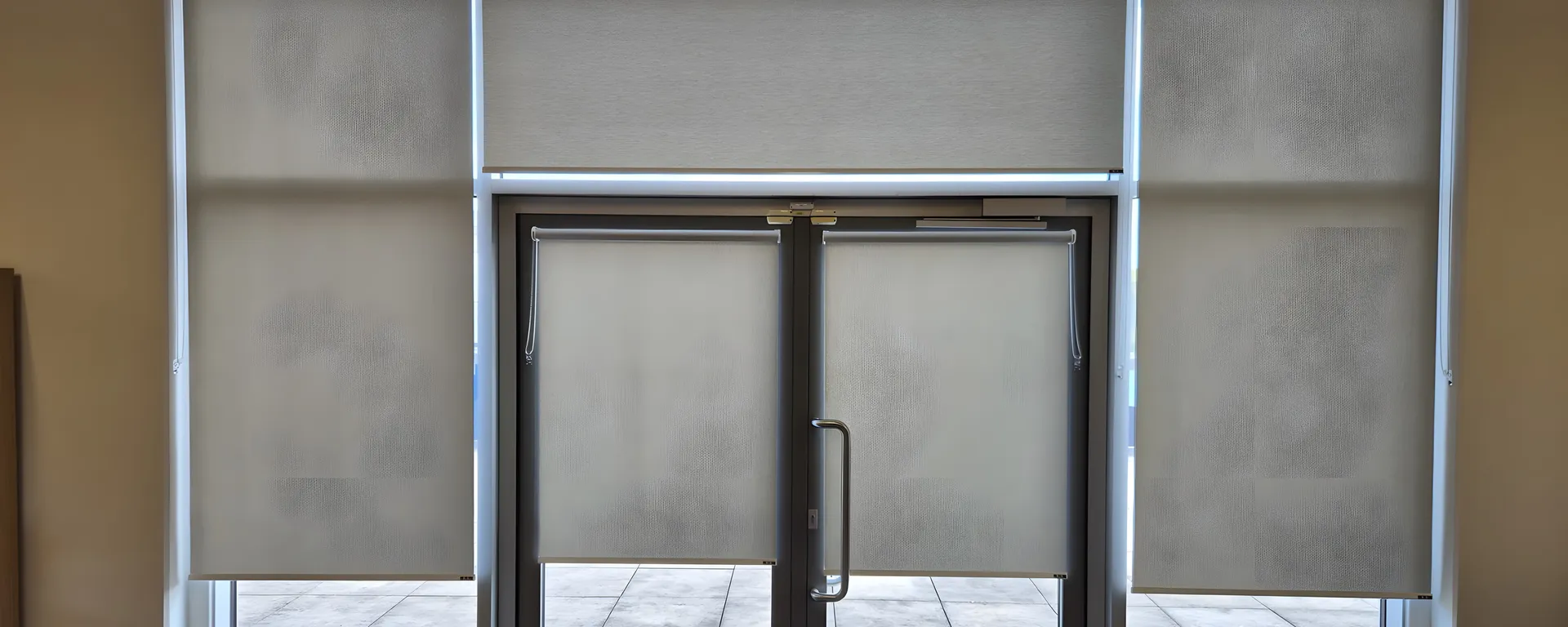 Wall of matching dim-out roller blinds either side of a glazed fire exit door at Moorside High School