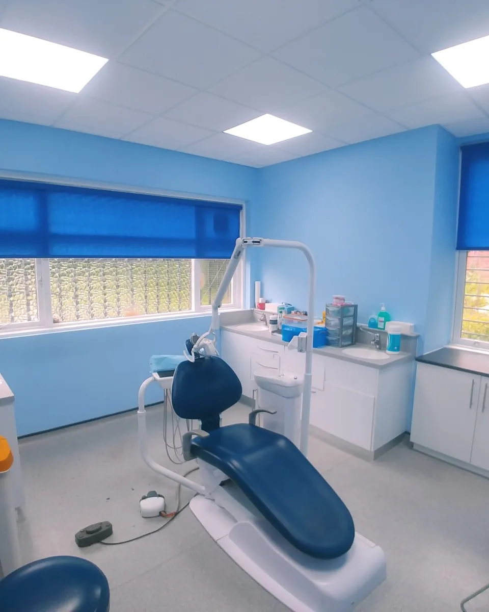 Blue roller blinds on two windows of a dental treatment room in North Manchester, with the dental chair in the middle of the room