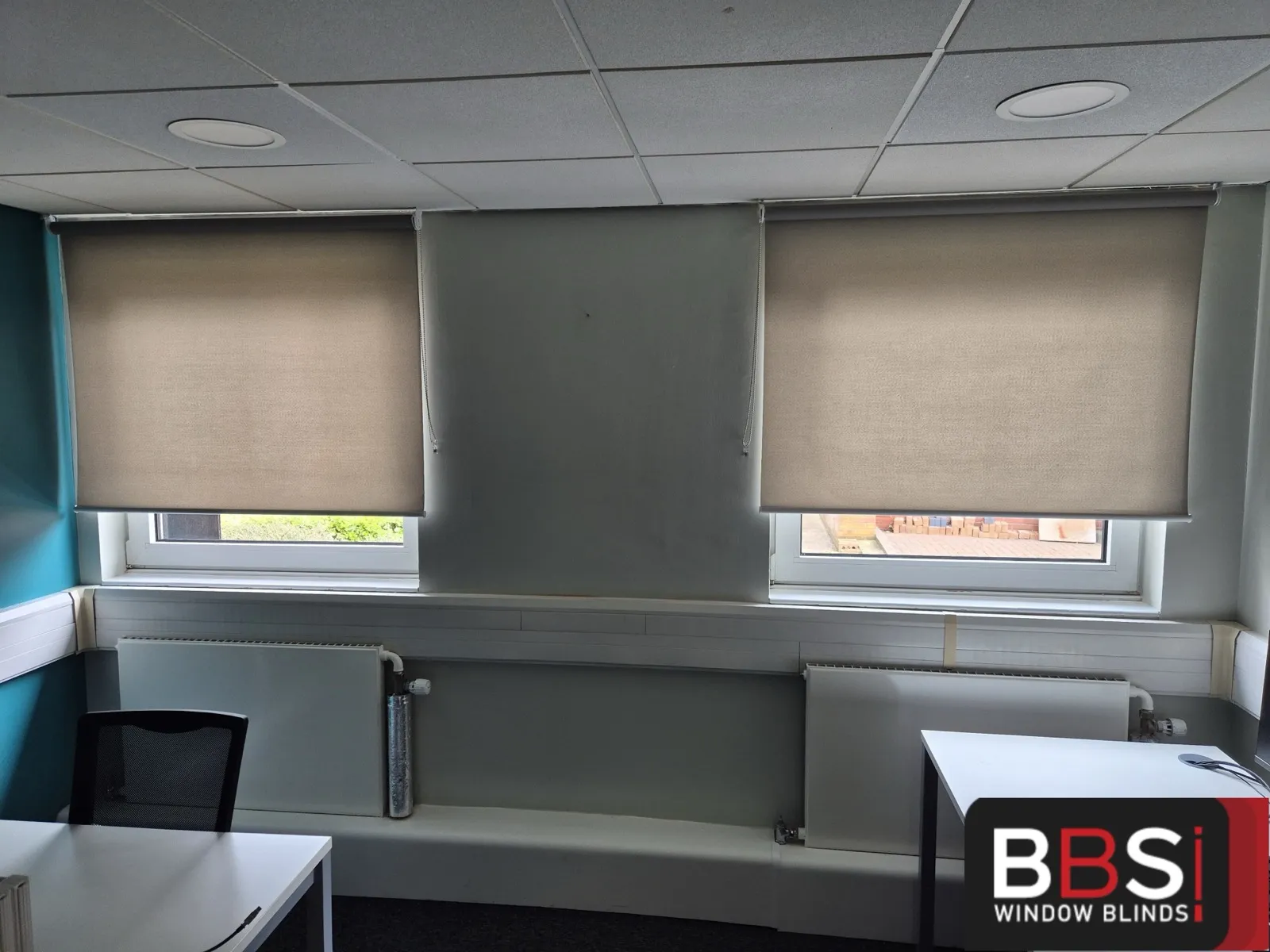 Two matching roller blinds fitted above a shared desk run in an NWAS office