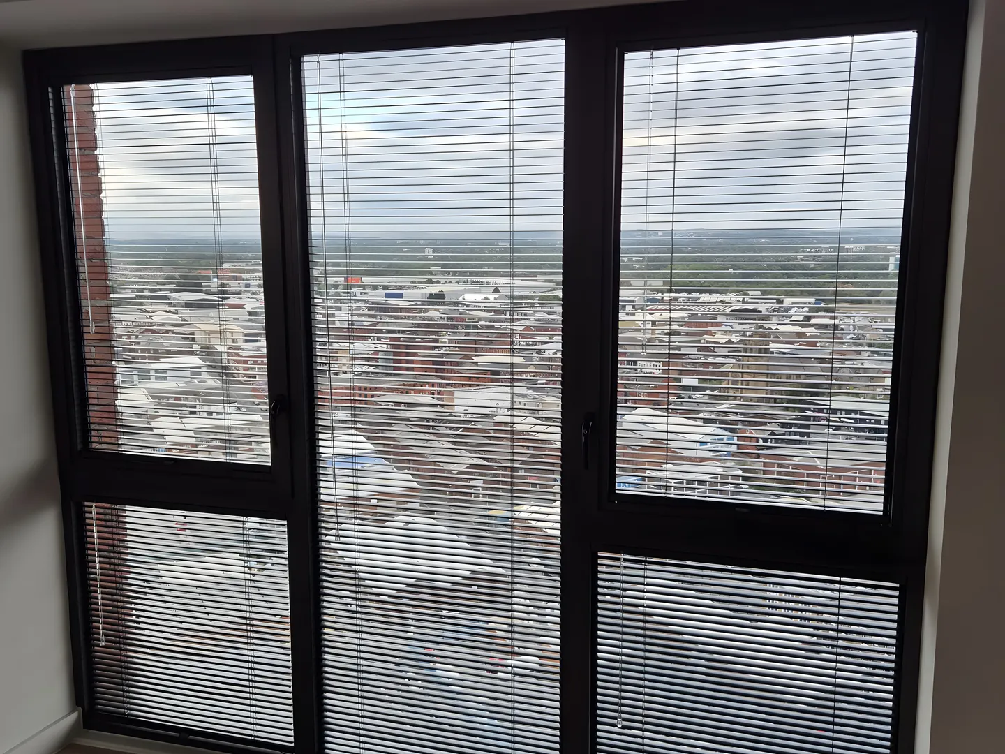 Perfect Fit Venetian blinds on a tall corner window looking out over Manchester rooftops