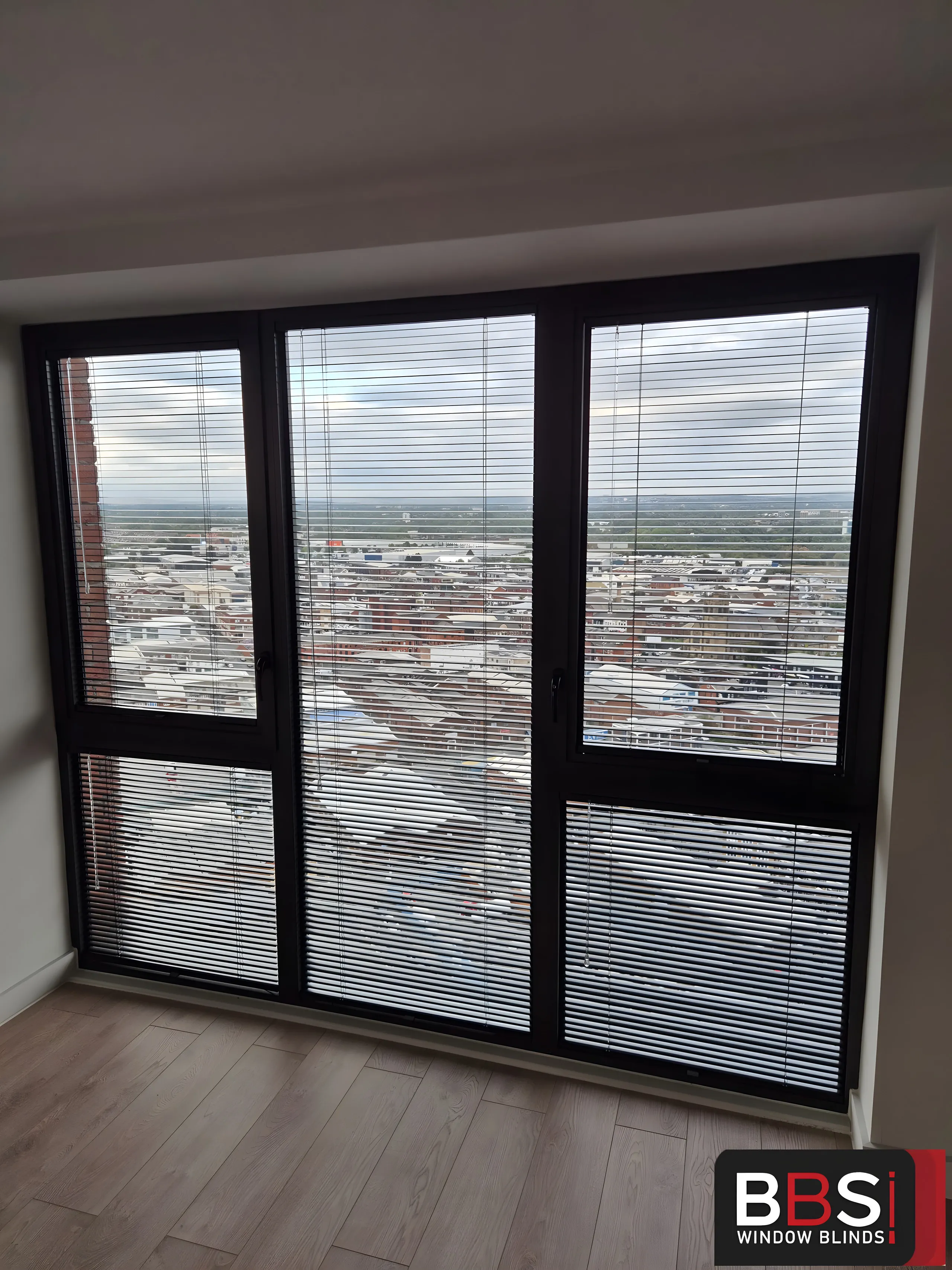 Perfect Fit Venetian blinds on a tall corner window looking out over Manchester rooftops