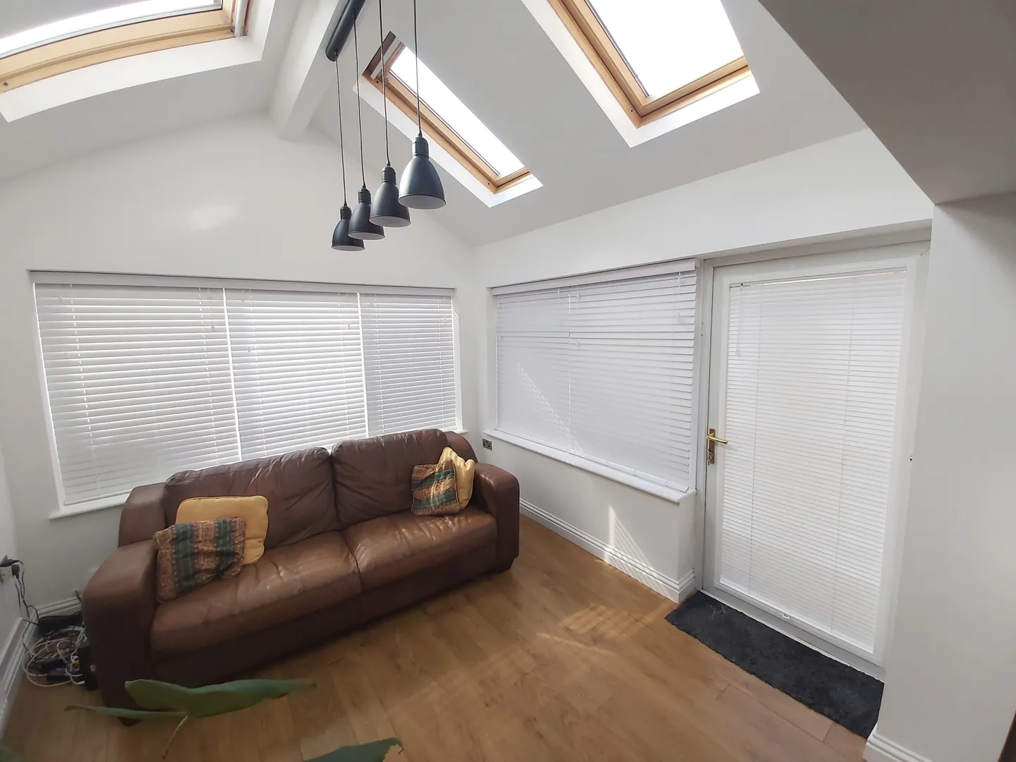 White Venetian blinds on every pane of a conservatory with a brown sofa