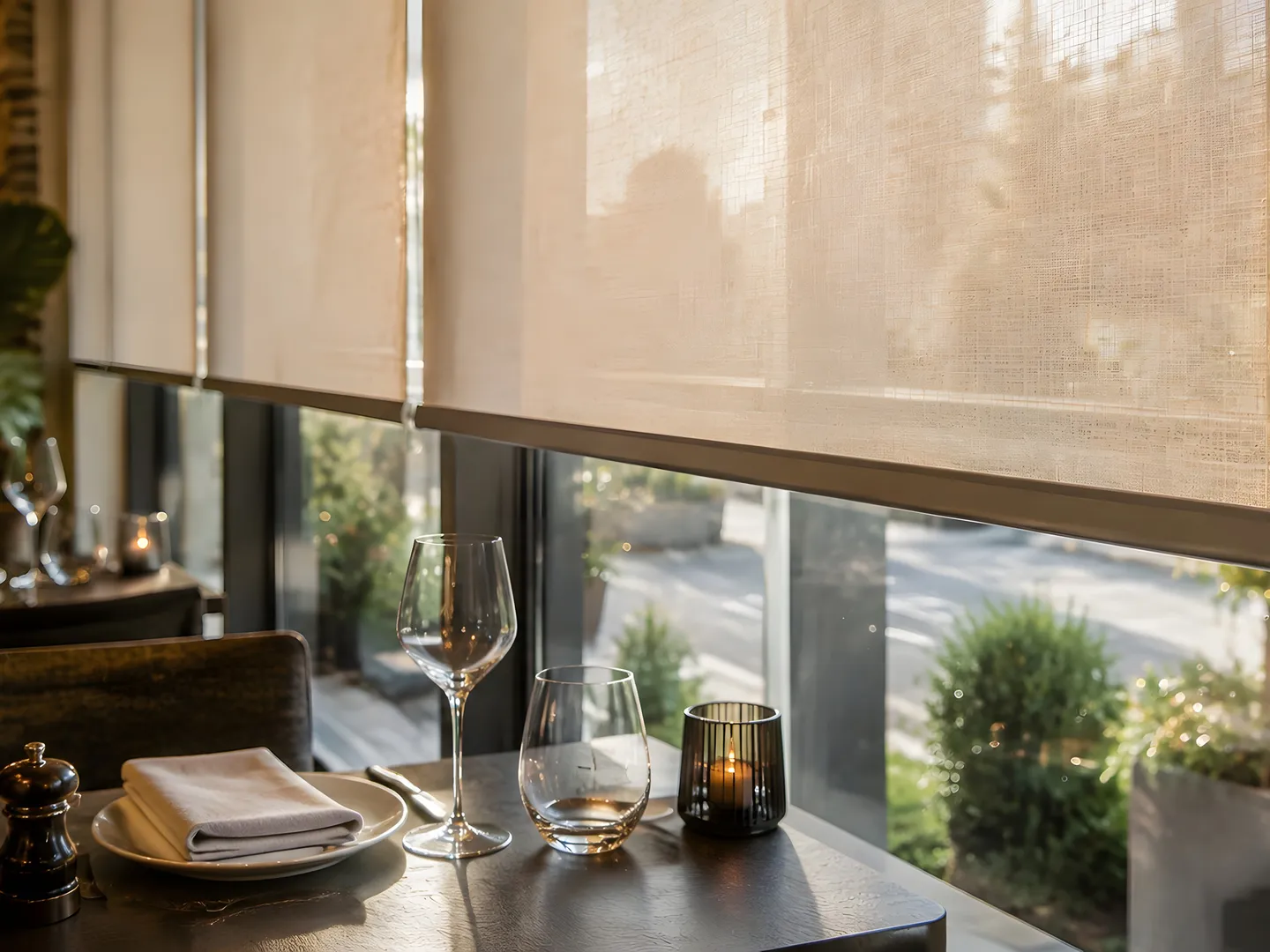 Textured roller blinds beside neatly set street-facing restaurant tables