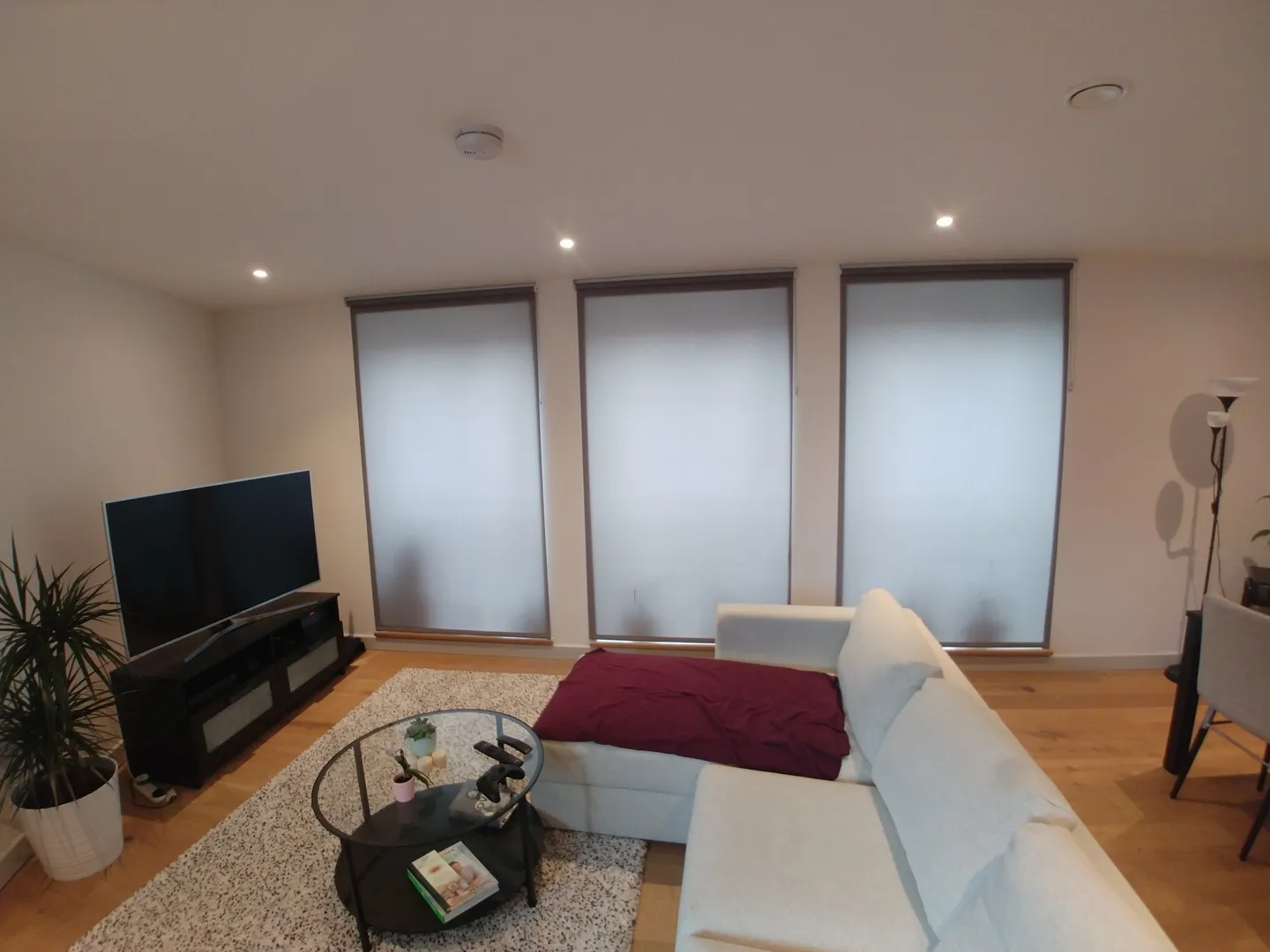 White roller blinds on the windows of a new-build apartment living room with a corner sofa