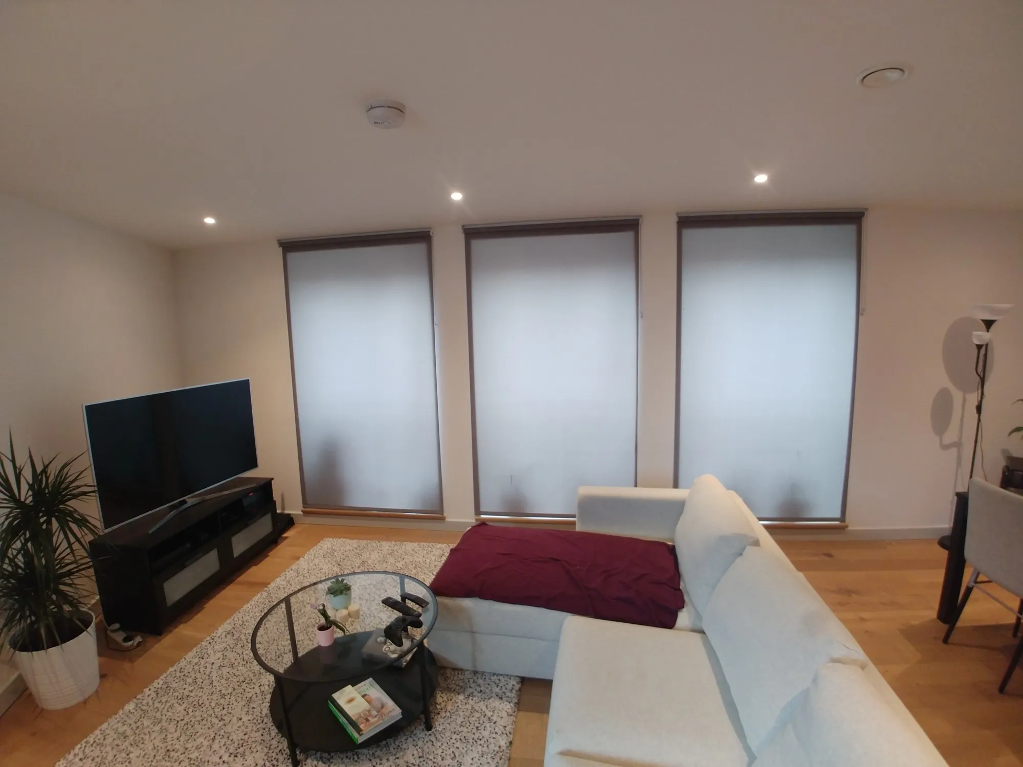 White roller blinds on the windows of a new-build apartment living room with a corner sofa