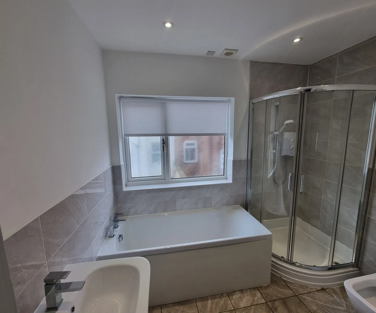 Grey roller blind at a bathroom window between the bath and a walk-in shower