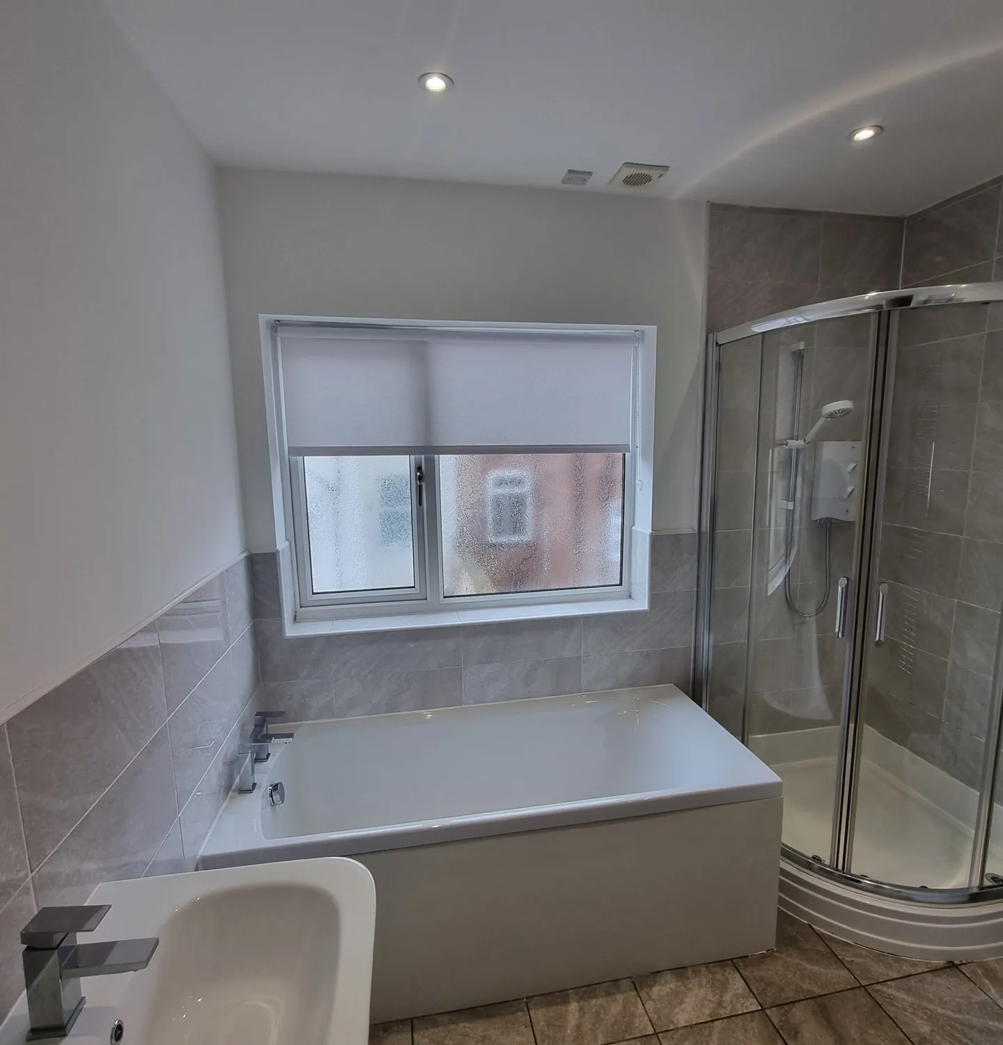 Grey roller blind at a bathroom window between the bath and a walk-in shower