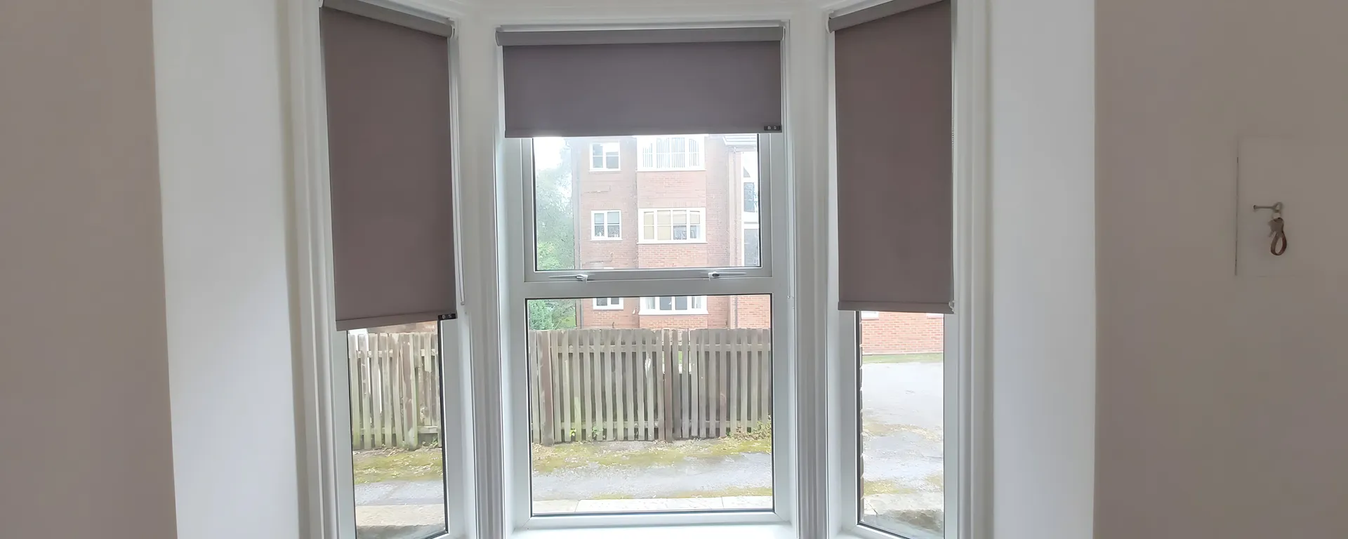 Three grey roller blinds fitted to the sash windows of a period bay in a Manchester home